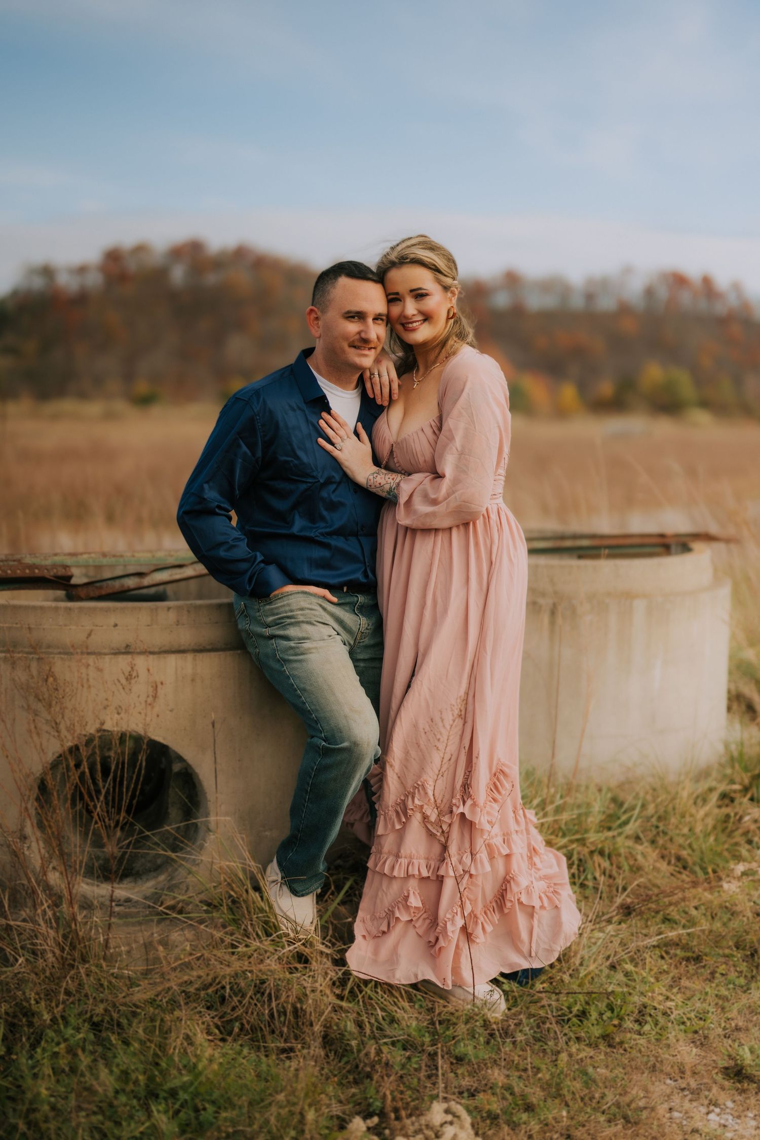 A romantic couple poses together against a rustic backdrop wearing coordinated fall outfits.