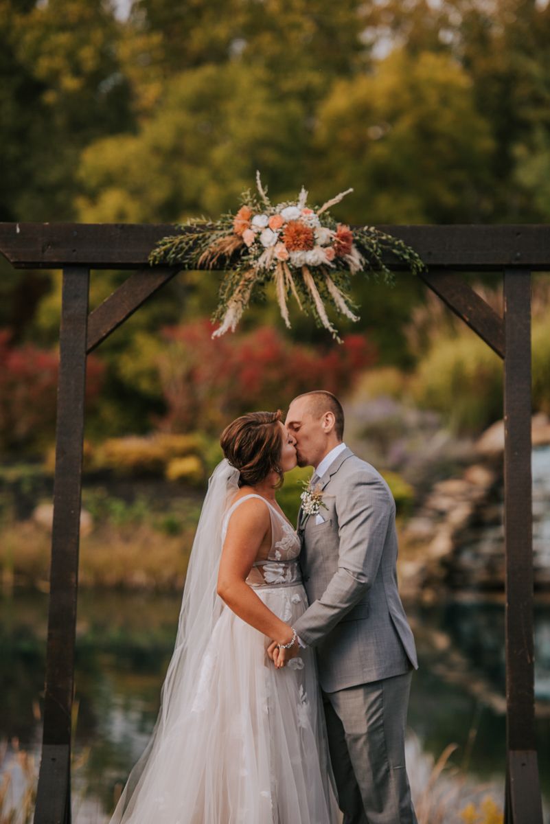 A romantic wedding moment under a wooden arbor surrounded by autumn foliage.