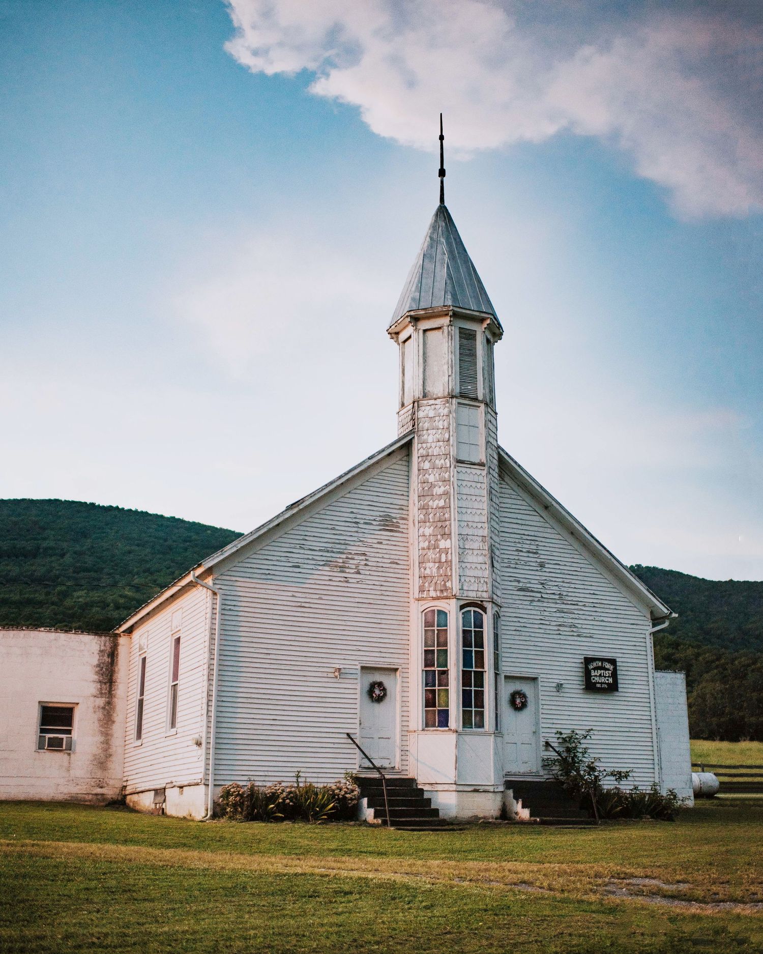 White country church with steeple photographed from different angles against mountain backdrop.