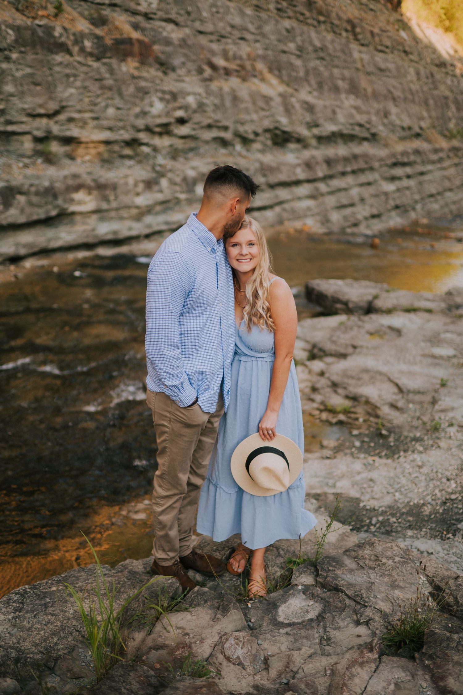 A romantic moment captured on rocky terrain near a waterfall with soft natural lighting.