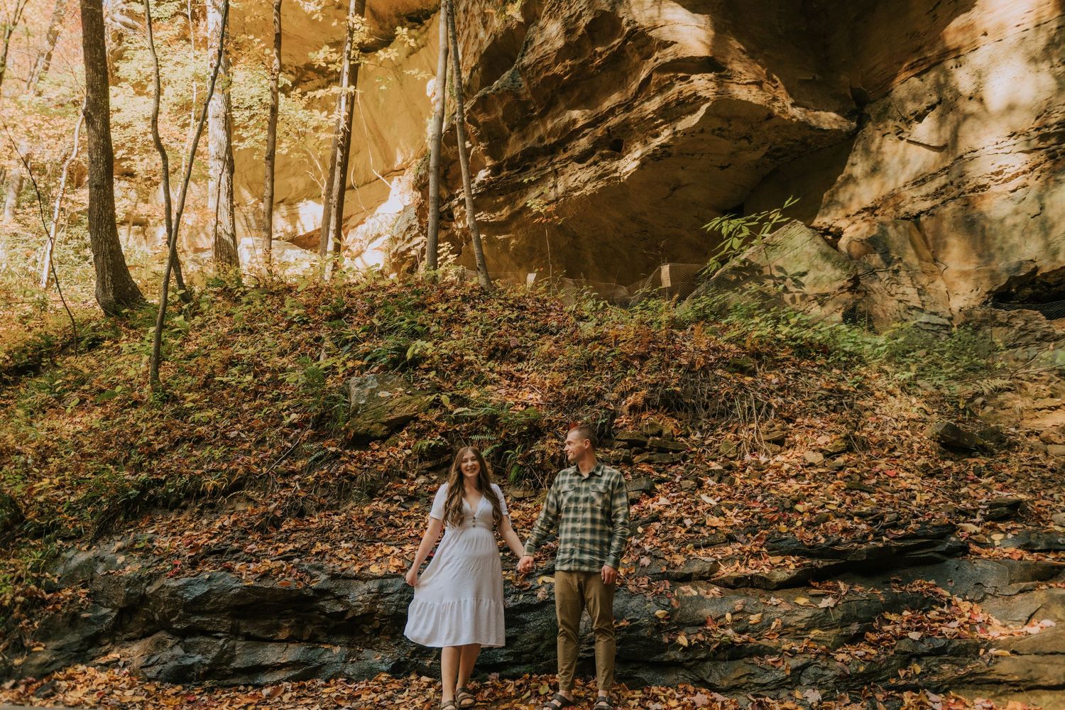 Engagement photo beneath towering rock formations in autumn woodland setting.