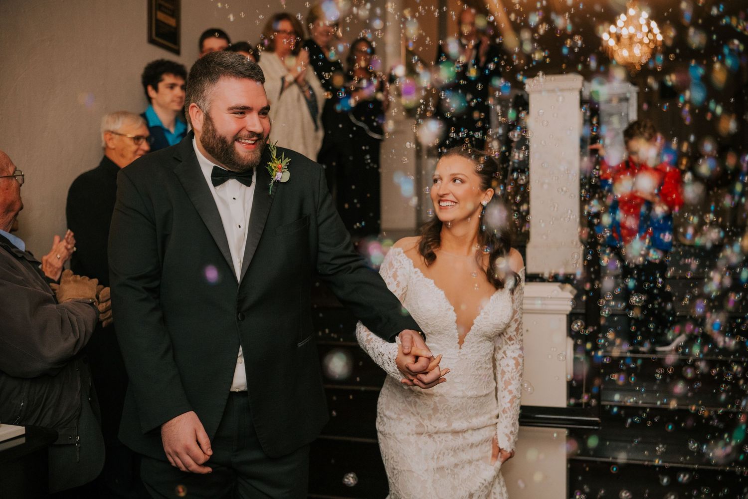 Newlyweds walk hand in hand through falling confetti at their indoor winter wedding celebration.