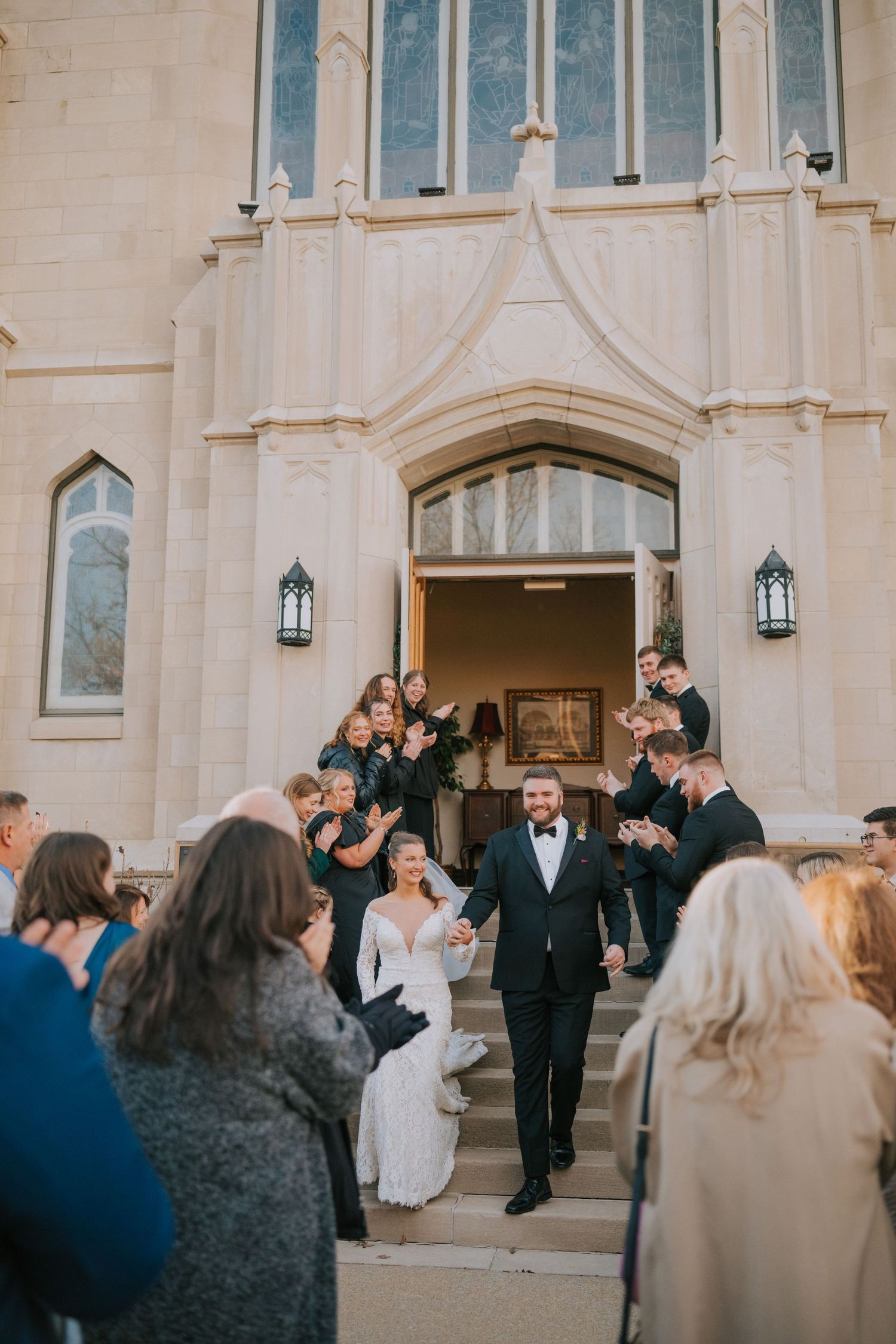 Newlywed couple exits a church while guests celebrate their emergence on the steps after a winter wedding ceremony.