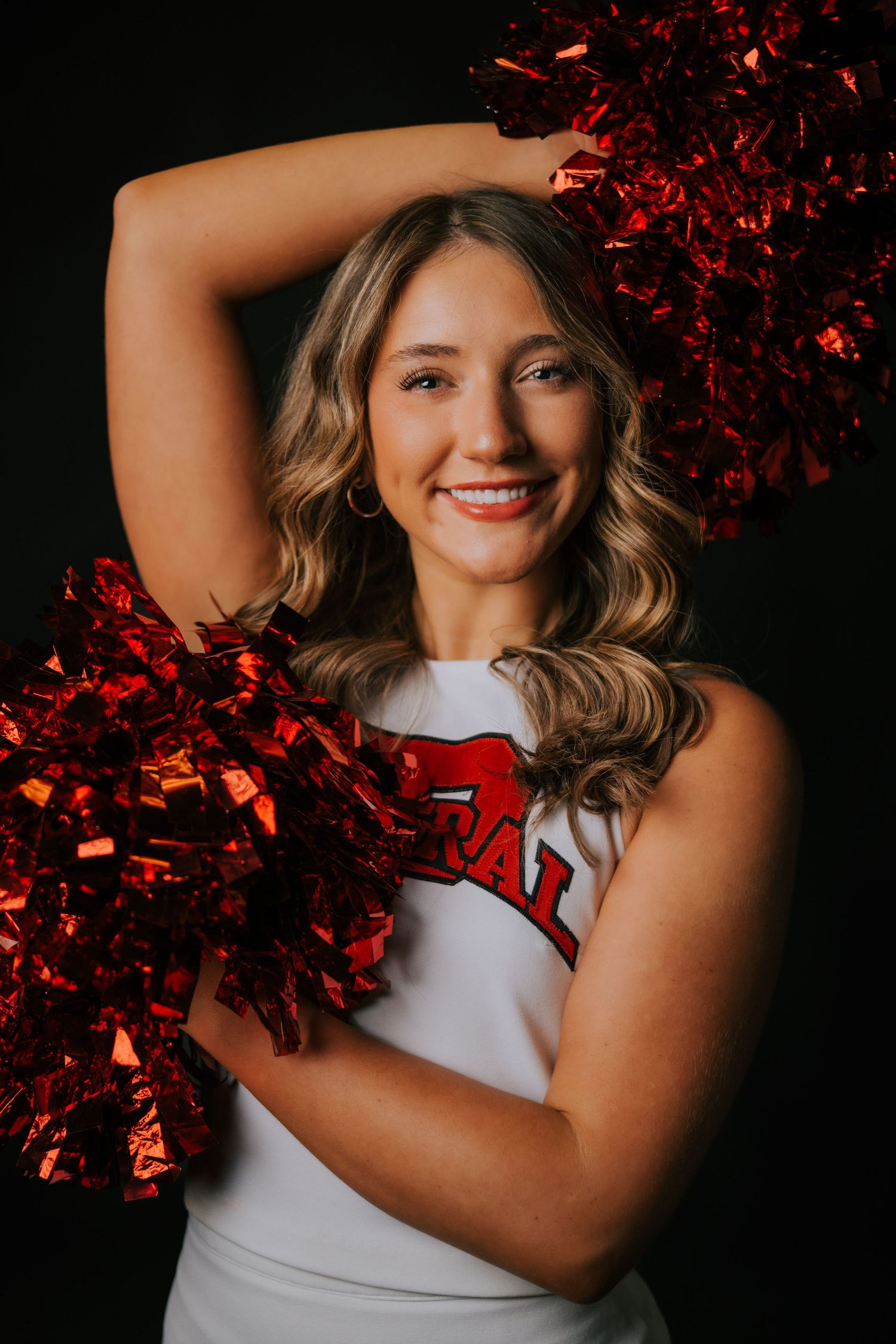 Cheerleader in white uniform holds red metallic pom poms against dark background in dynamic photo series.