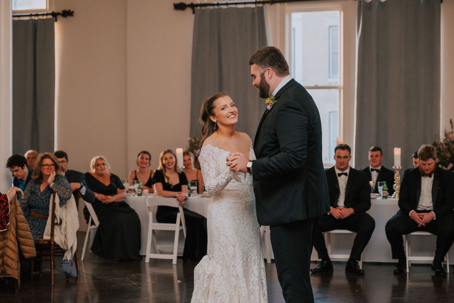 A couple shares their first dance at an elegant indoor wedding reception surrounded by guests.