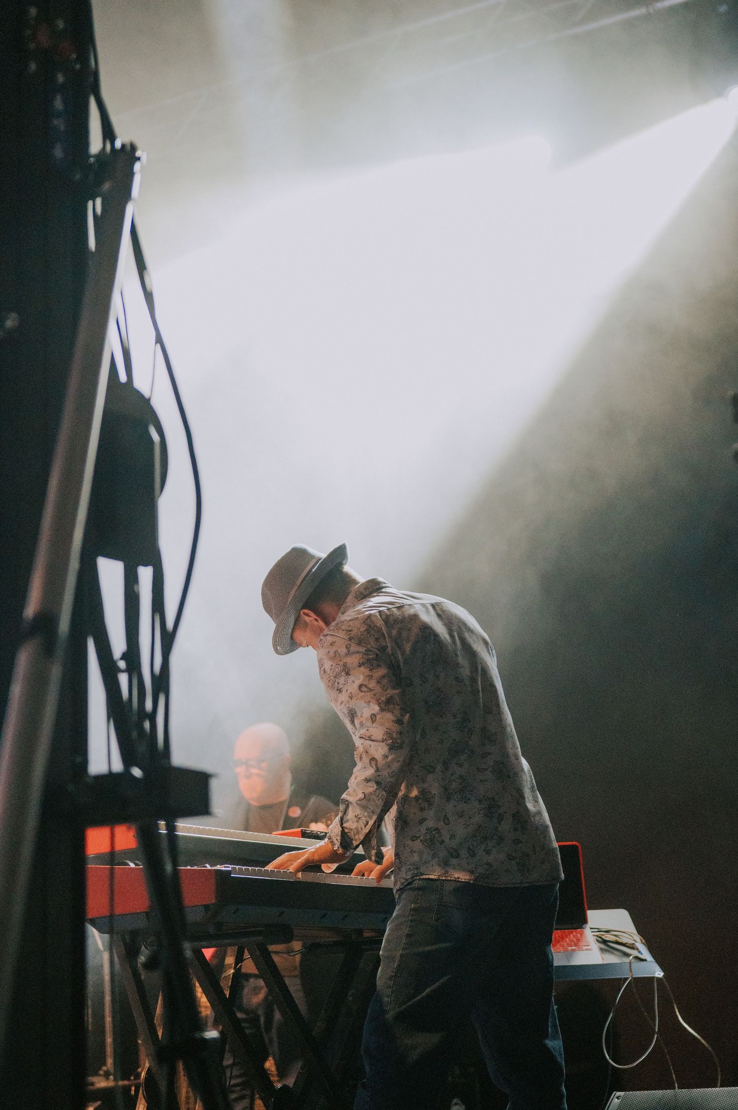 Musician performing on keyboards under dramatic stage lighting and fog effects.