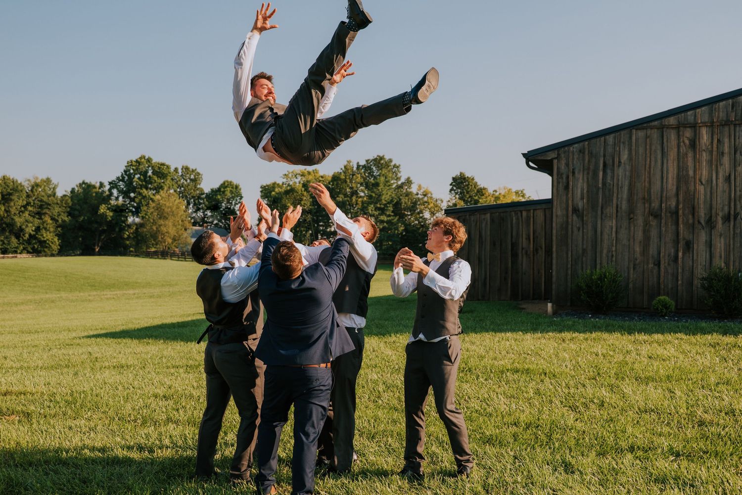 Wedding party performs playful group poses on a grassy field.