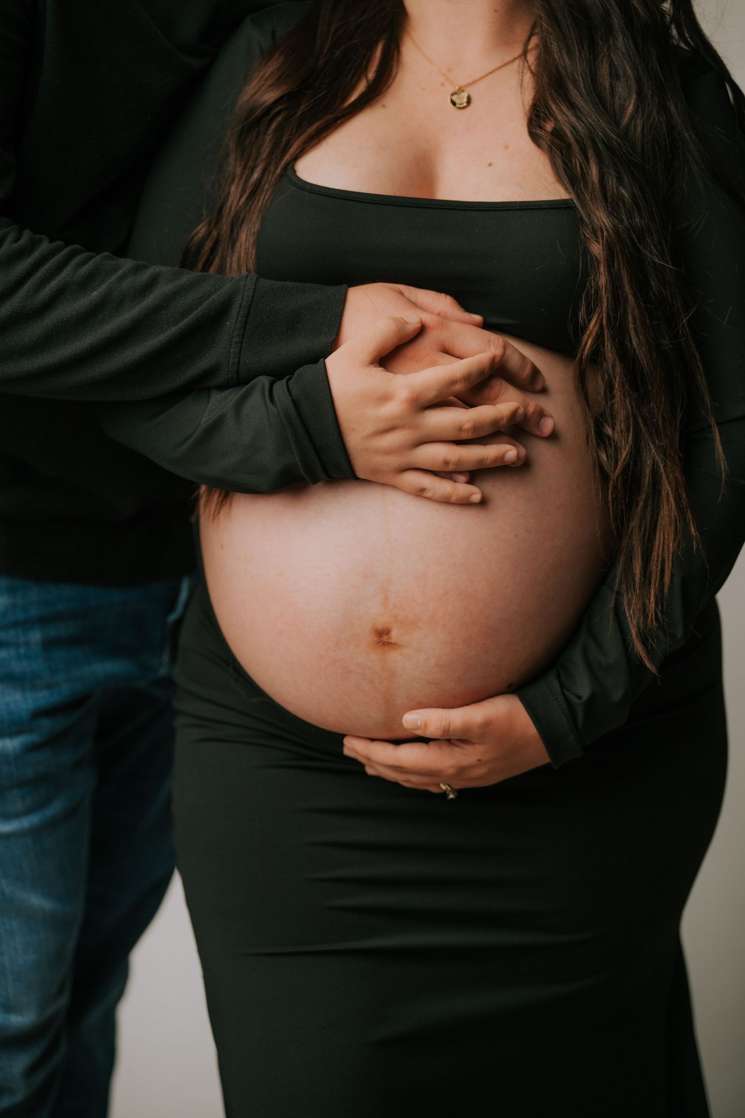 Close-up series of a pregnant belly in a black top with hands gently cradling it.