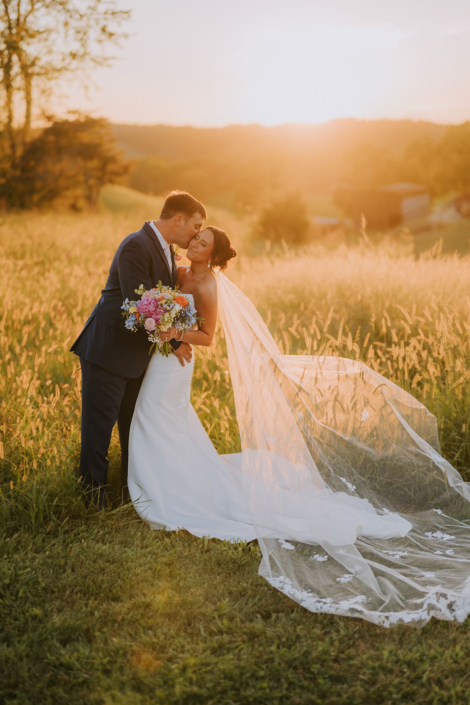 Romantic sunset wedding photo in a golden field with flowing white dress and veil.