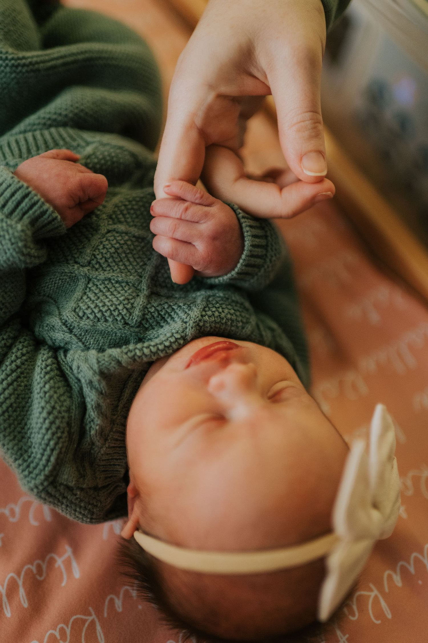 Close-up of tiny baby feet in green knit sweater being held by gentle hands.