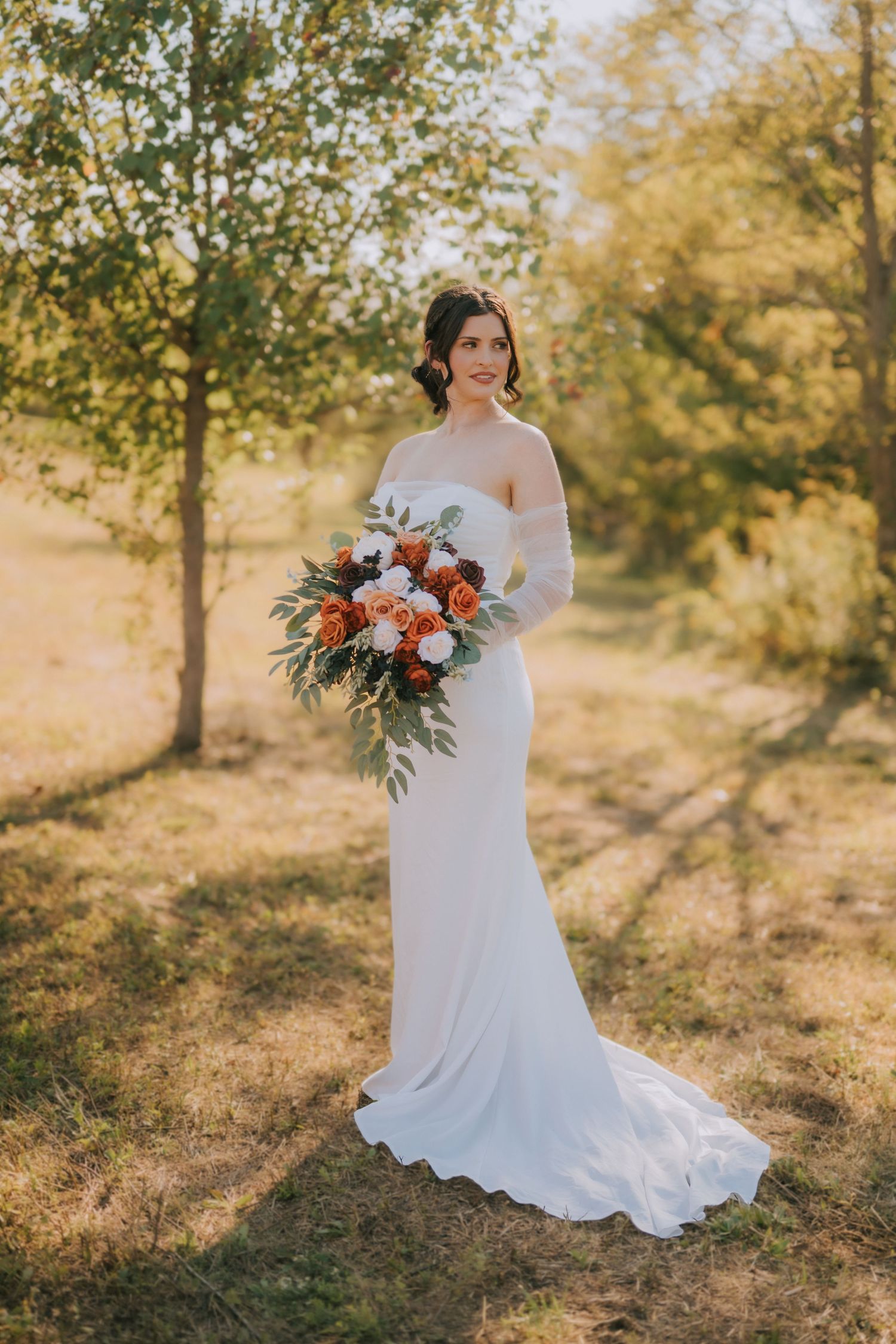 Bride in flowing white gown holds colorful bouquet during autumn outdoor bridal session.