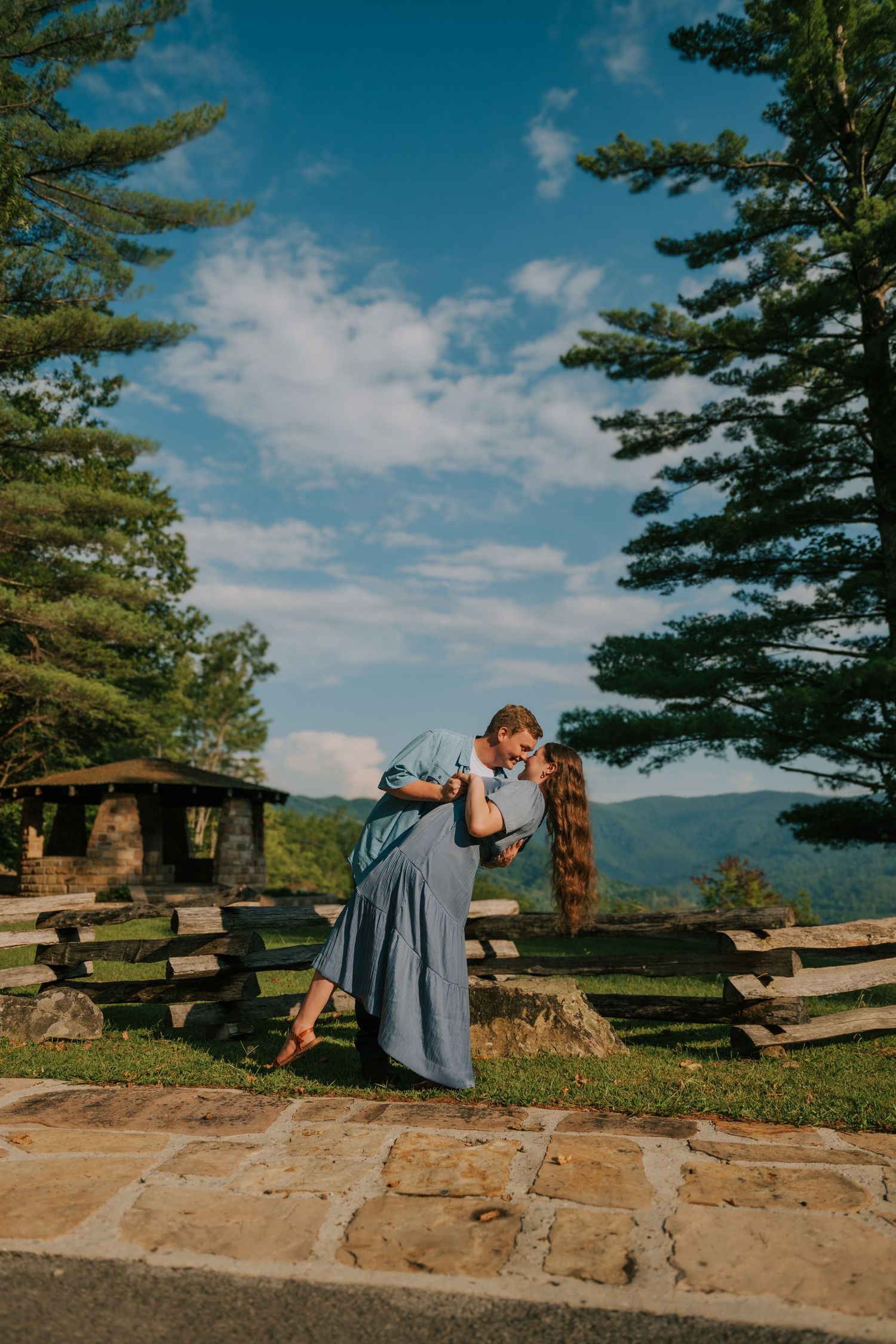 A scenic mountain overlook with blue skies and evergreen trees on a stone observation area.
