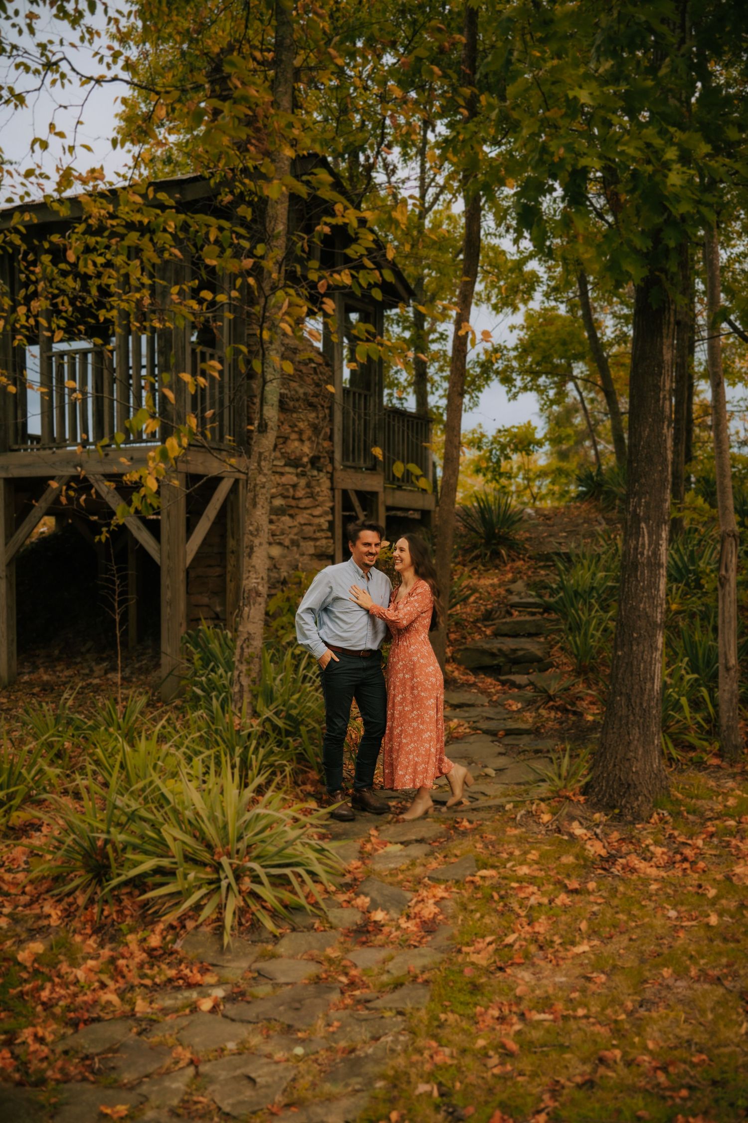 A couple shares a romantic autumn moment among fallen leaves and trees at sunset.