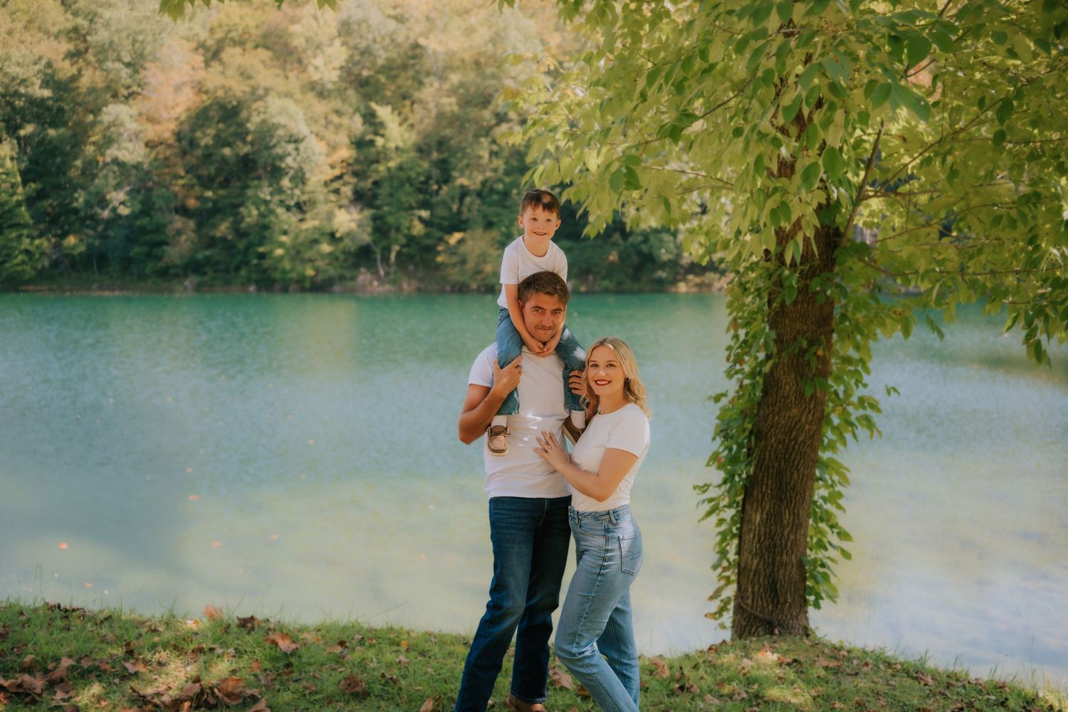 A family moment captured by a serene lake with autumn trees in the background.