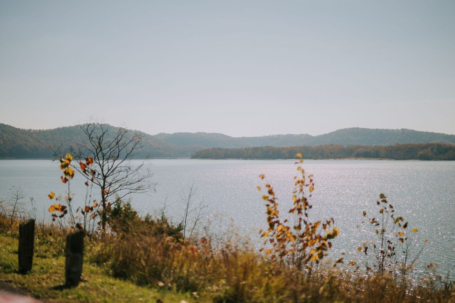Panoramic view of a serene lake surrounded by mountains and autumn trees.