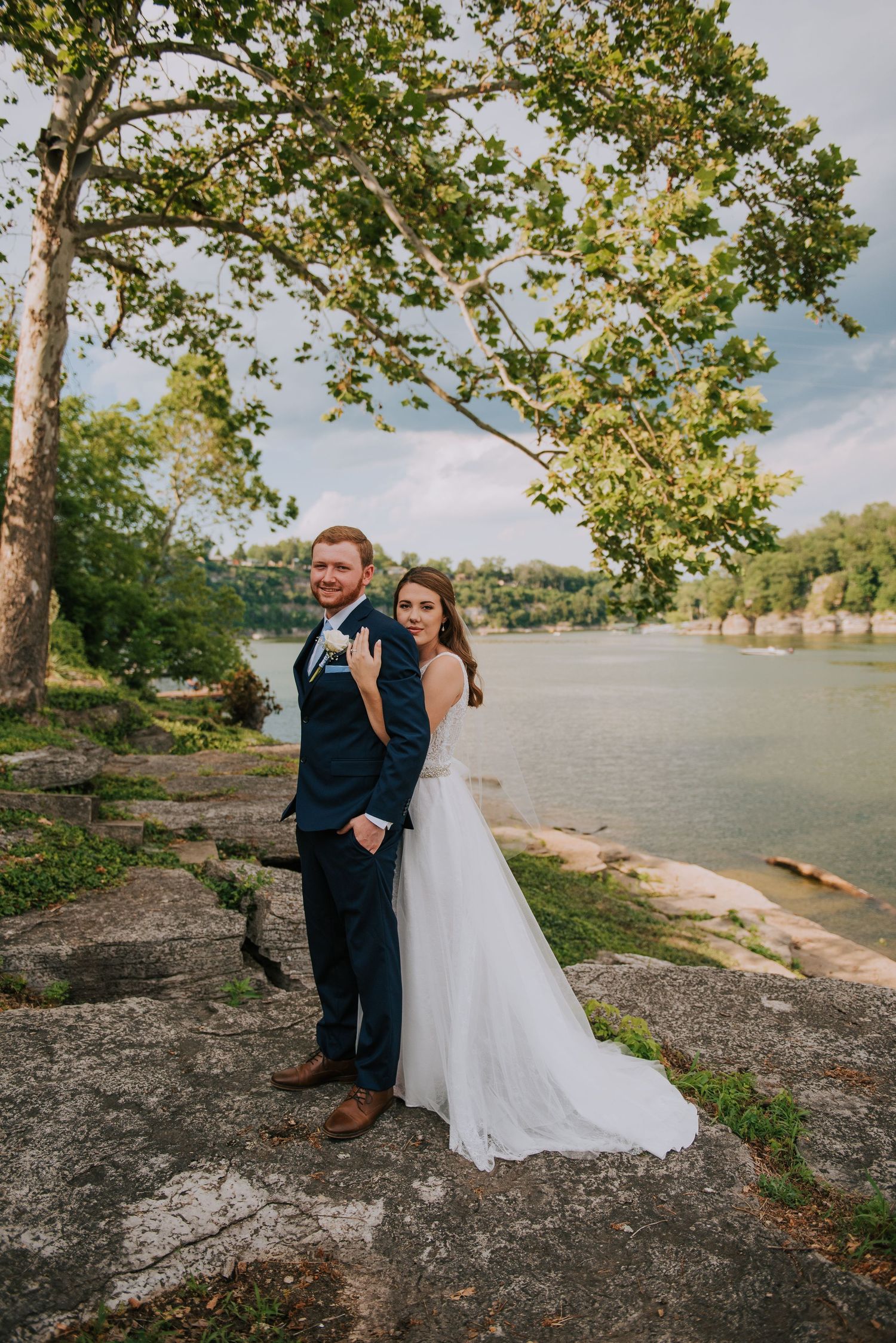 Wedding portraits captured along a scenic waterfront with trees and natural landscape.