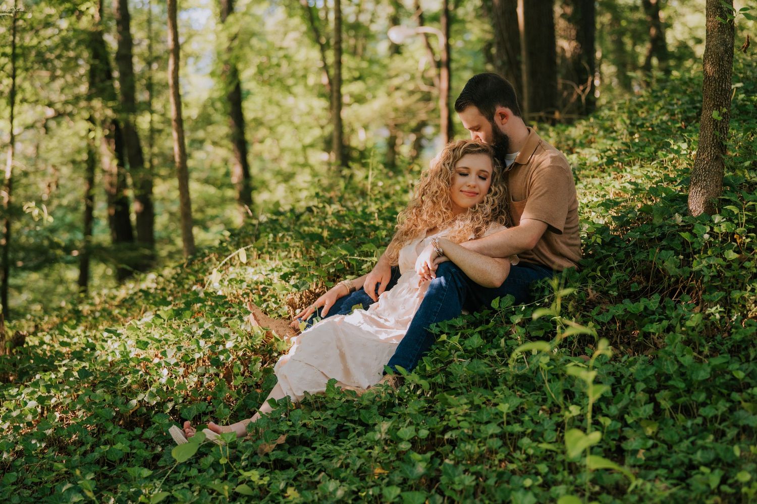 Couple shares intimate moments while lying in green forest foliage.