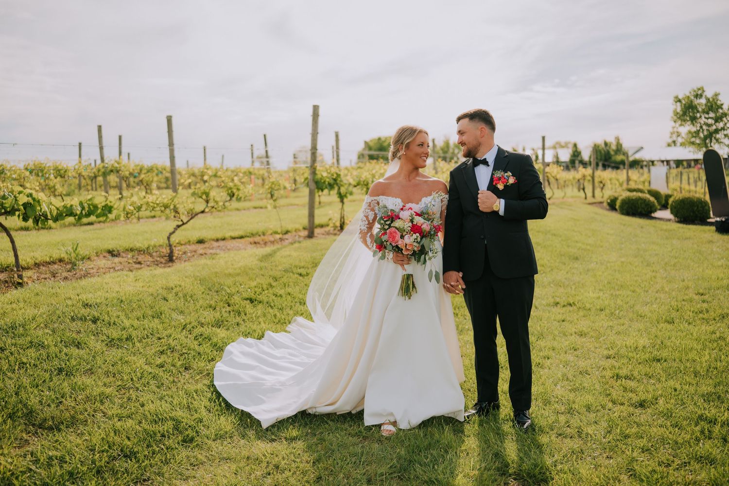 Wedding couple posing in vineyard with flowing white dress and classic black tuxedo.