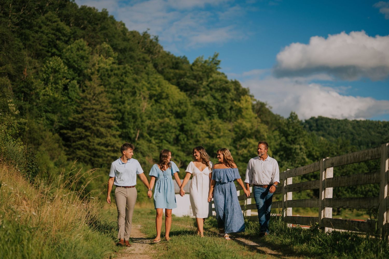 Group walking together along a scenic hilltop path with blue sky and clouds overhead.
