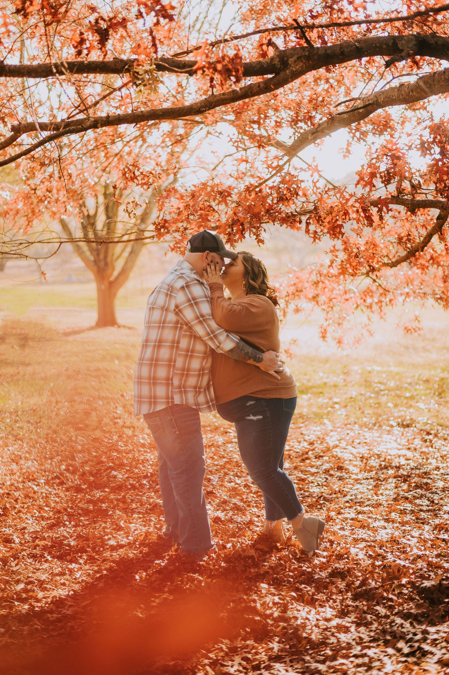 Romantic autumn photo session under trees with orange leaves and warm sunlight.