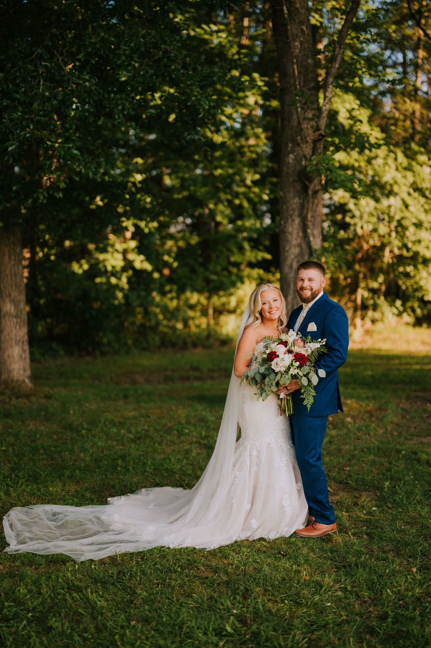 A romantic outdoor wedding photoshoot with a flowing white dress train on green grass.
