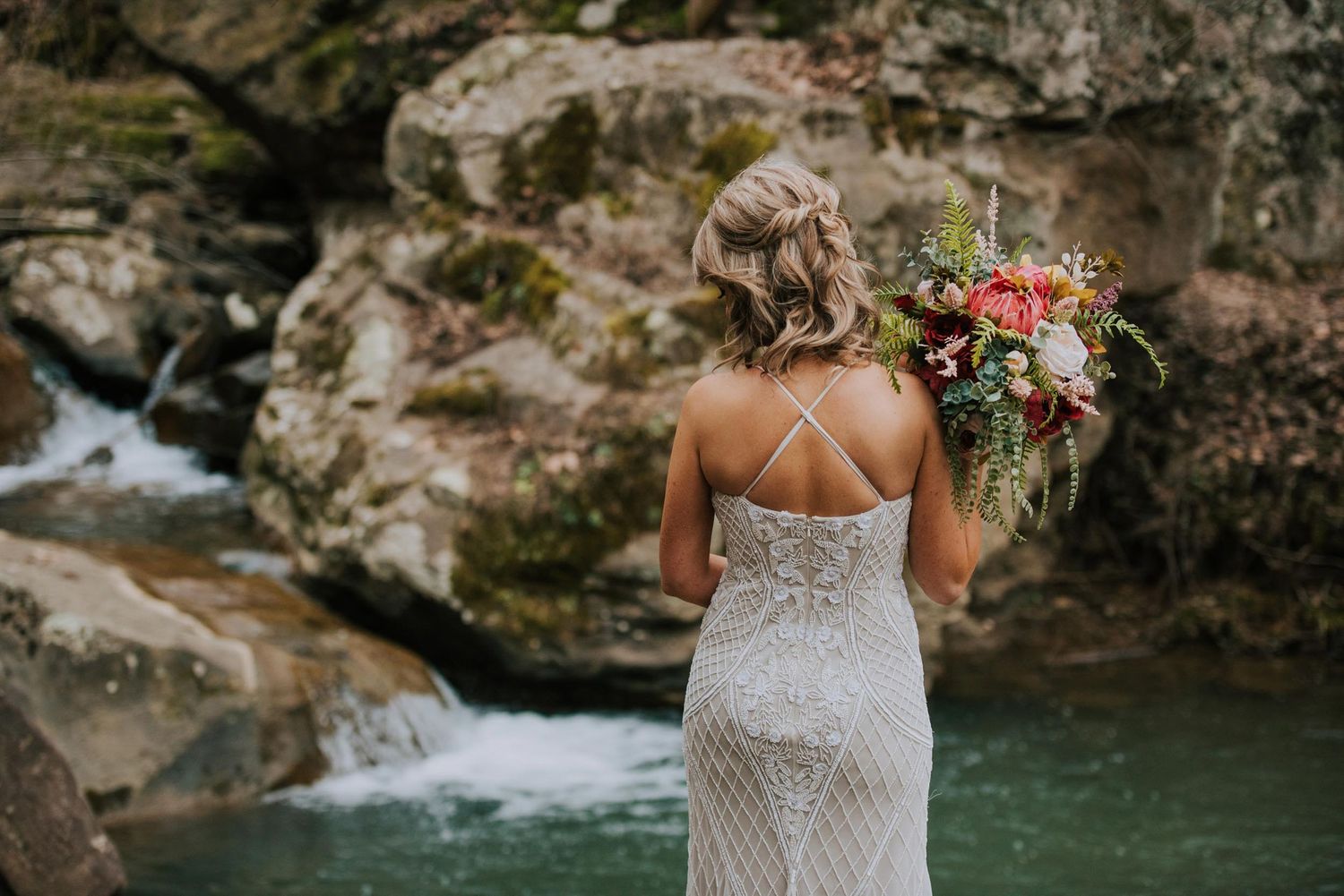 A couple poses near a scenic waterfall and rocky landscape on their wedding day.