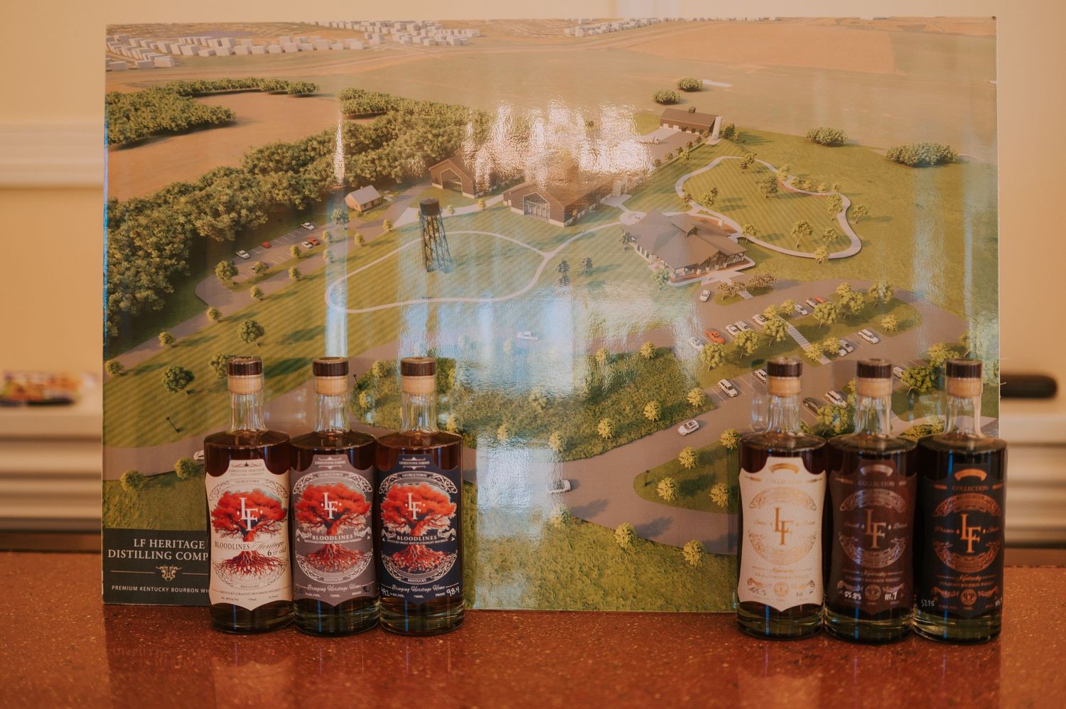Display of various liquor bottles arranged in front of a pastoral landscape painting or backdrop.