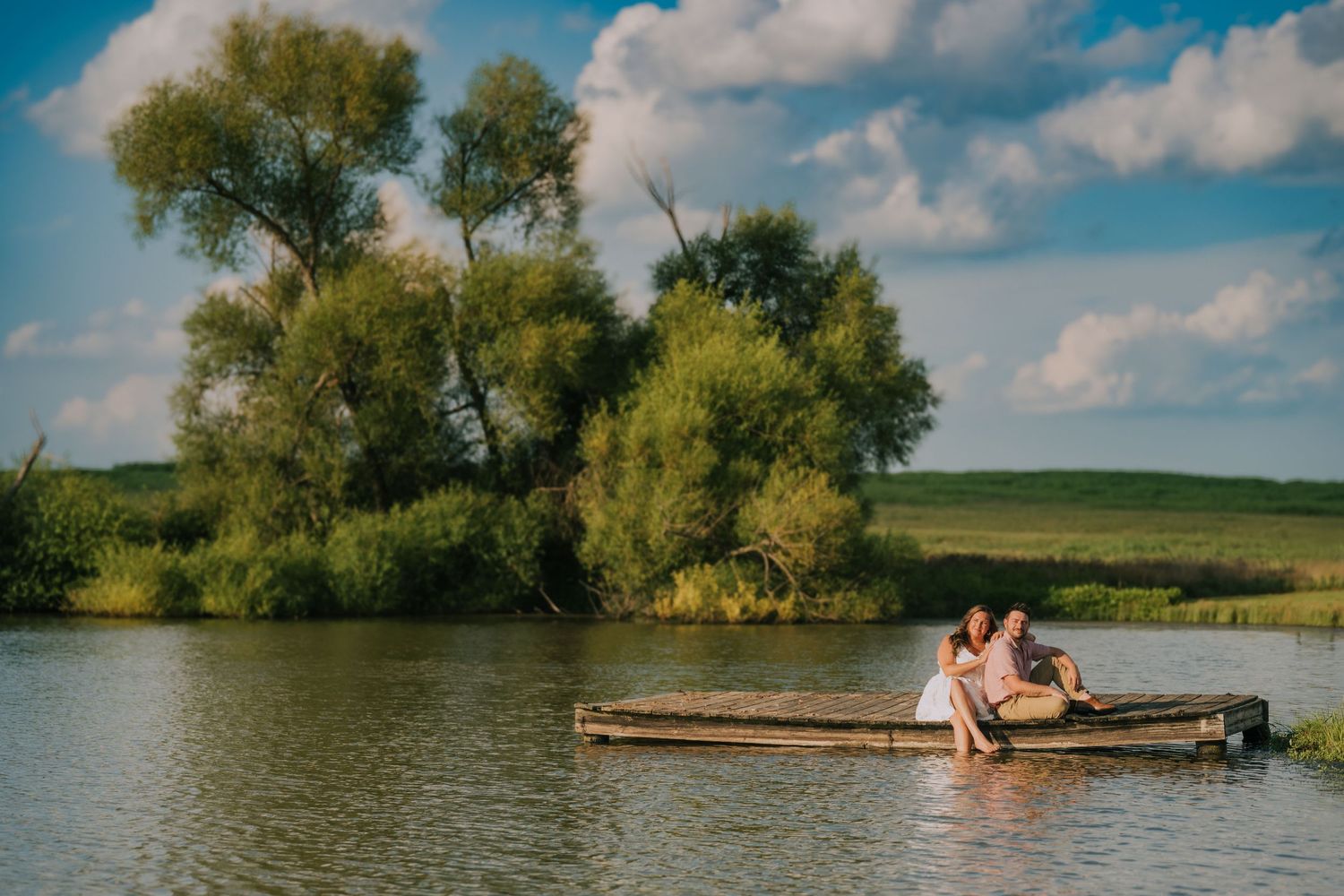 Couple relaxing on wooden dock by peaceful lake on sunny summer day.