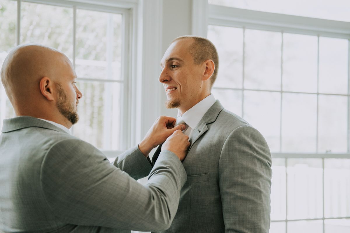Groomsmen in grey suits share emotional moment before wedding ceremony.
