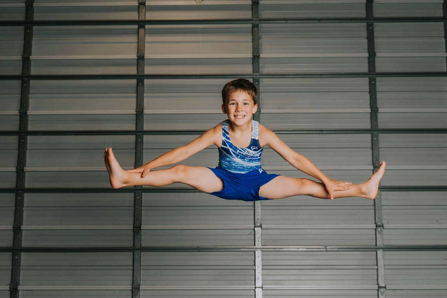 Gymnast performs split pose on parallel bars in indoor gymnasium.