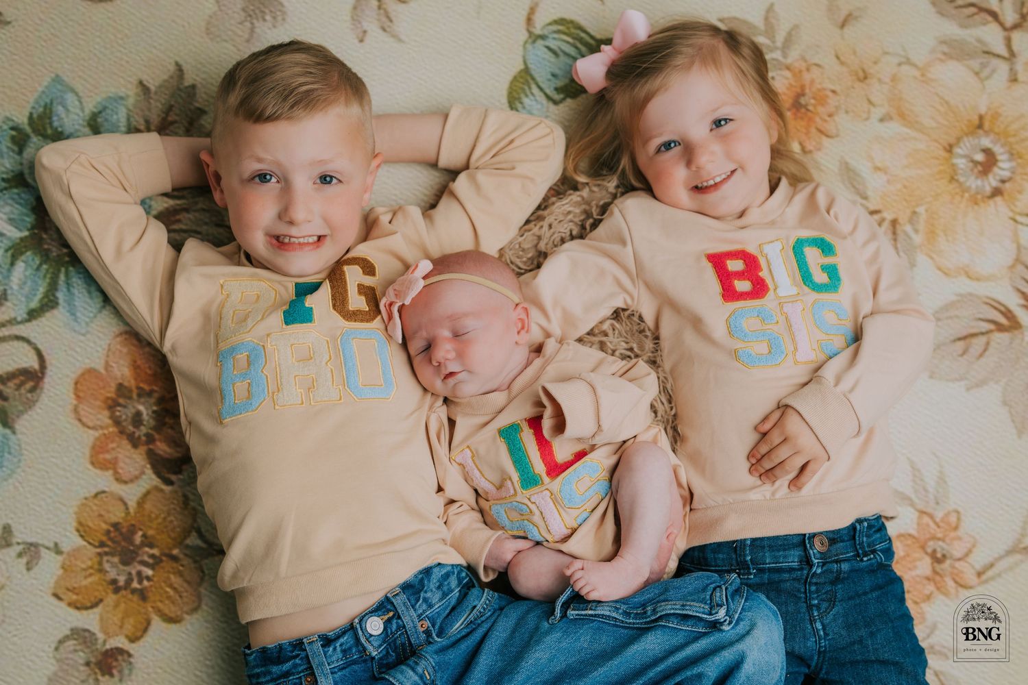 Children wearing matching outfits pose playfully on a floral patterned surface.