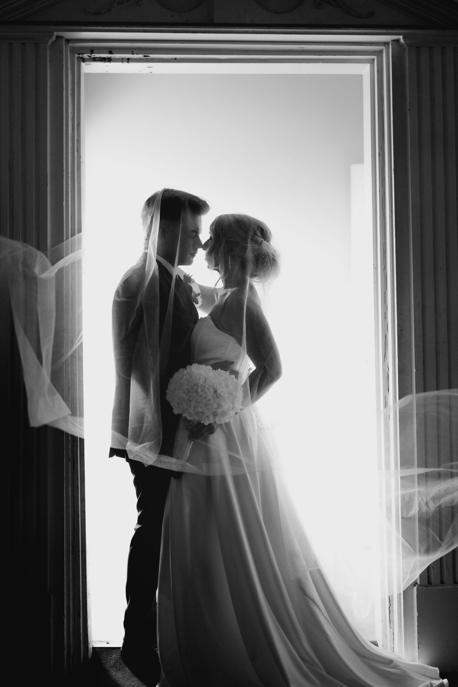 Silhouetted couple in wedding attire against bright window light.