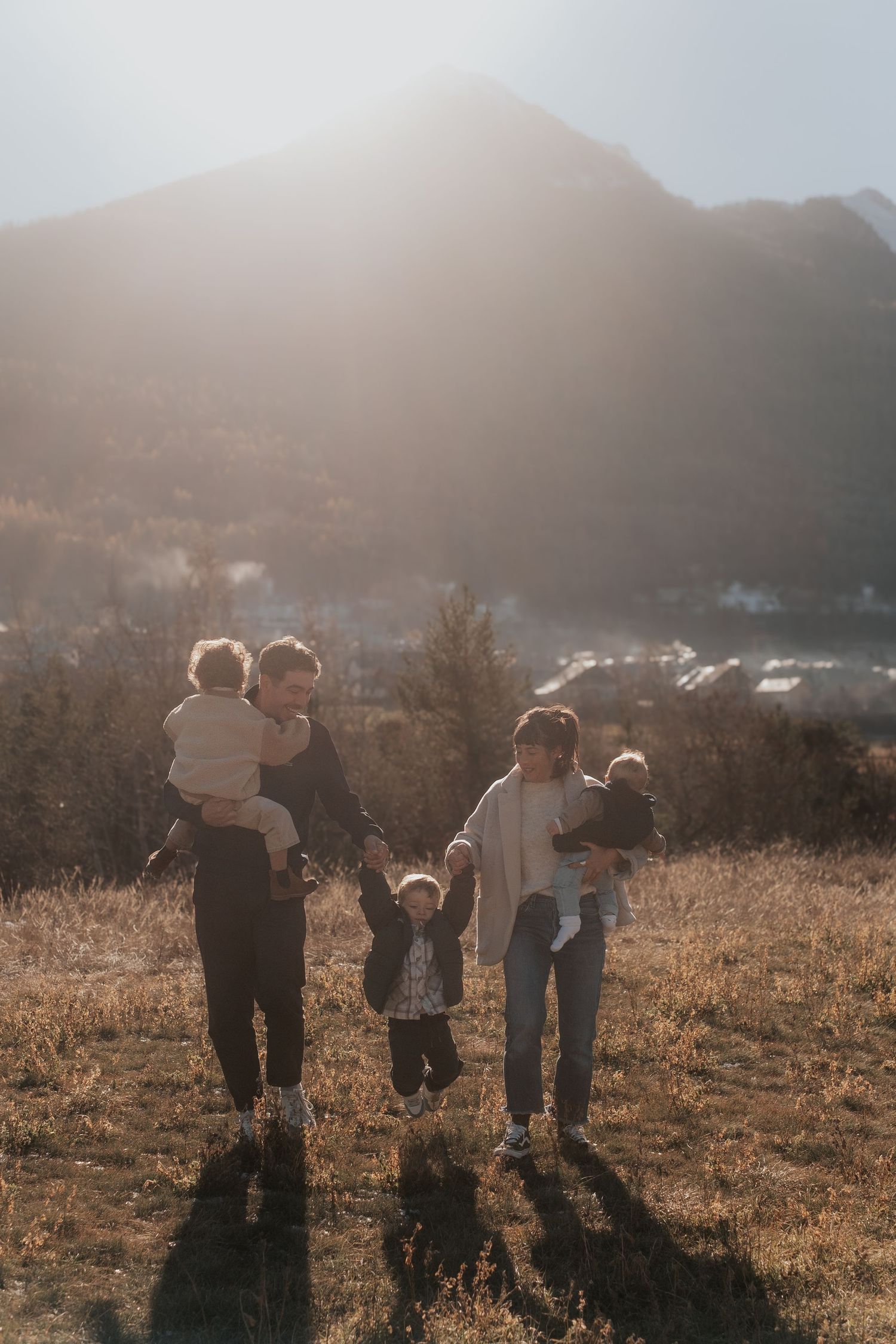 A group of people walking together on a grassy hillside during golden hour with mountains in the background.