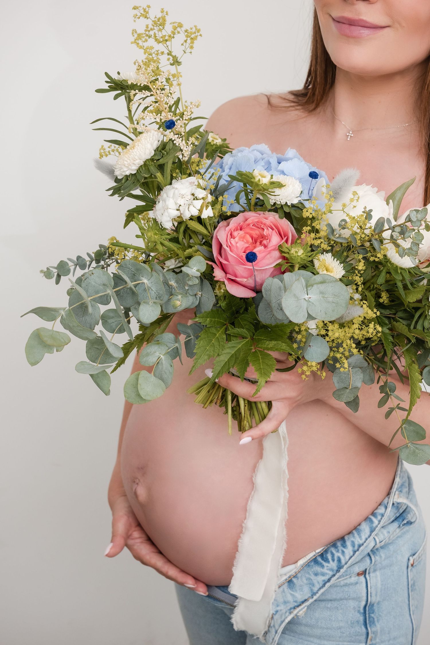 Beautiful floral arrangement with pink ranunculus, blue anemones, eucalyptus and white flowers against a light background.