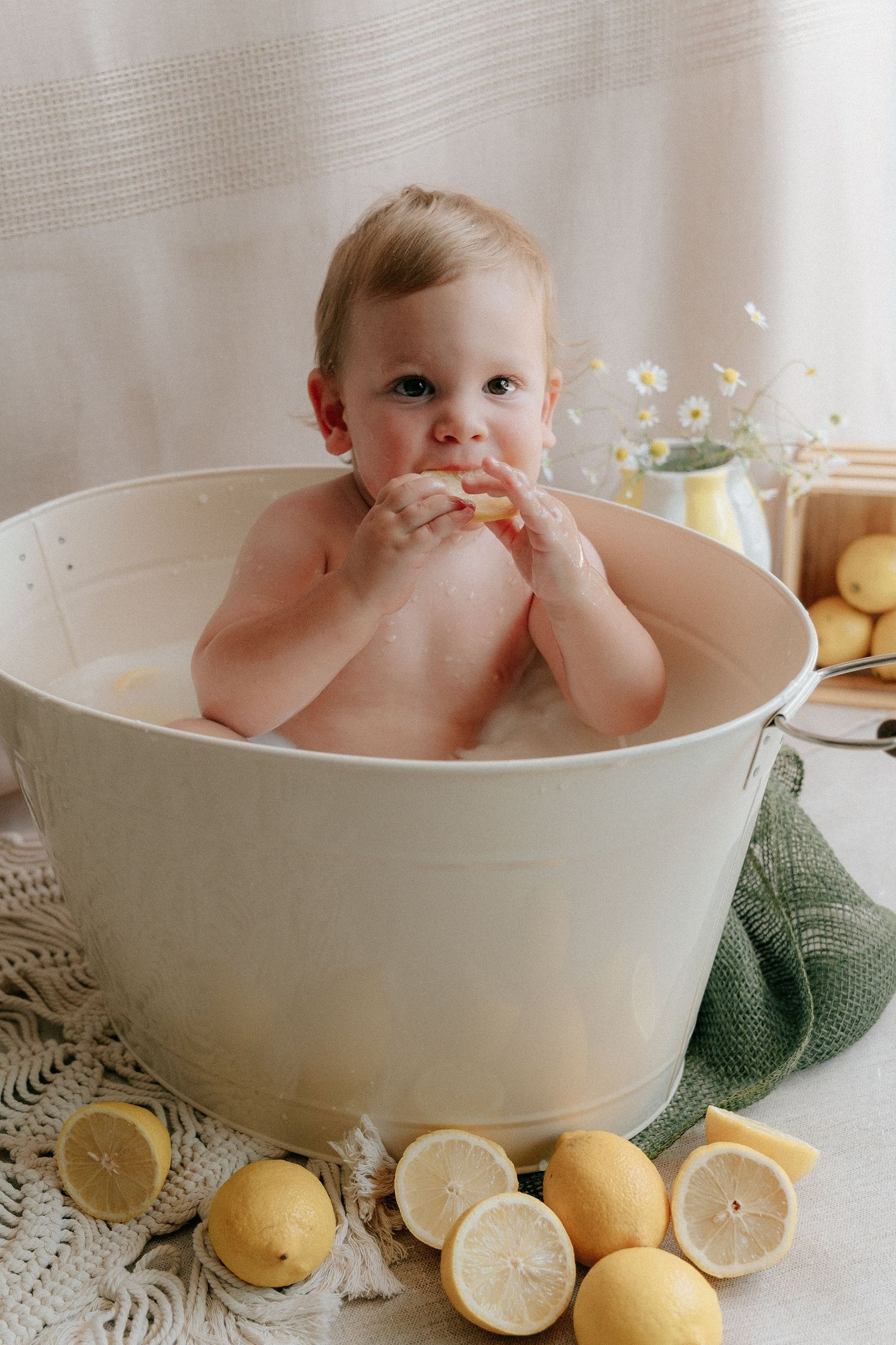 Baby bath time setup with lemons and white ceramic tub on lace doily.
