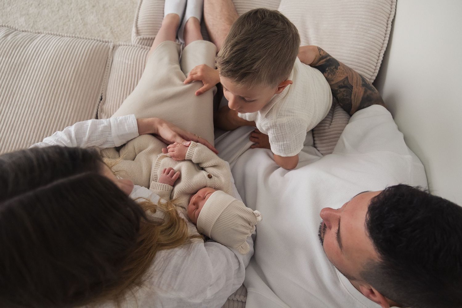 A series of tender moments between a parent and baby lying together on white bedding.