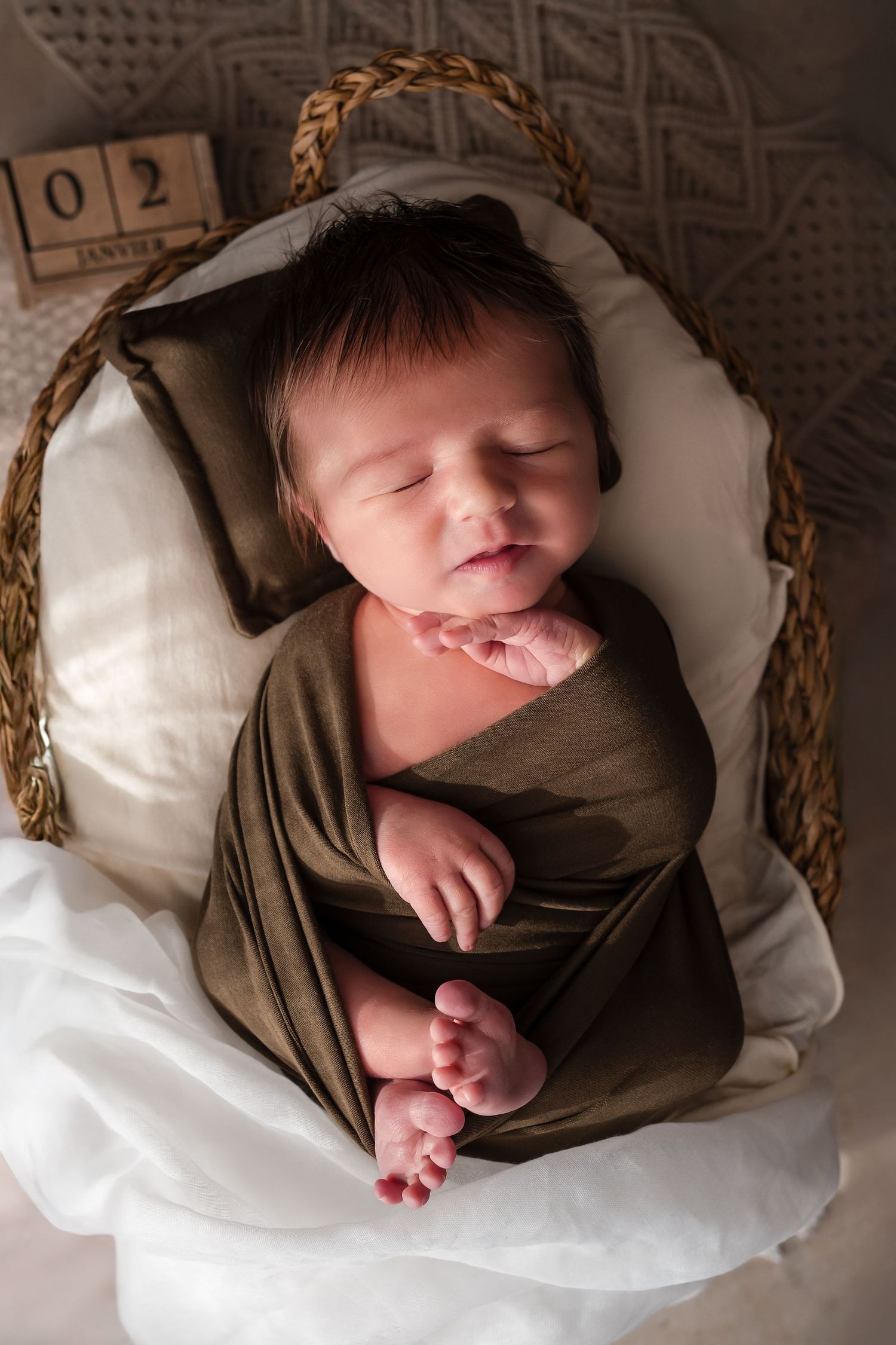 Newborn baby sleeping peacefully in white blankets and brown swaddle wrap, captured in multiple artistic angles.