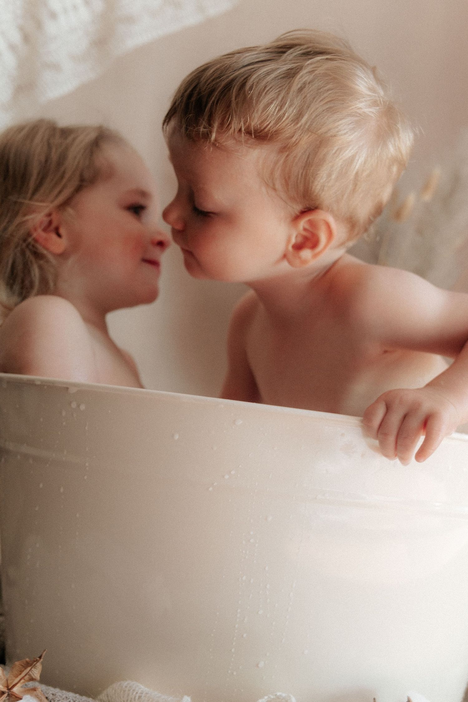 Two children sharing sweet moments in a white bathtub.