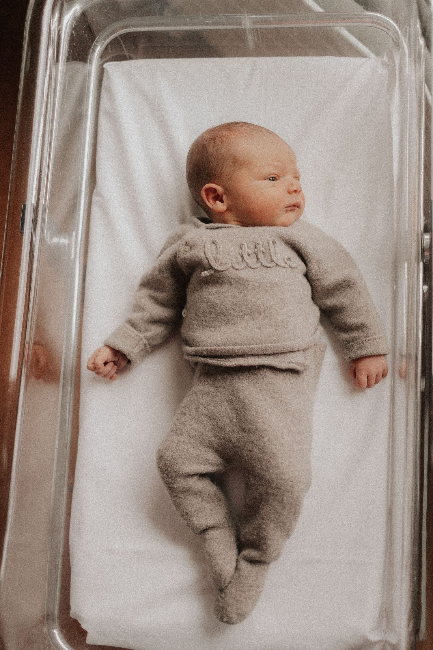 Sleeping newborn baby wearing cozy gray onesie lying on white bedding in multiple views.