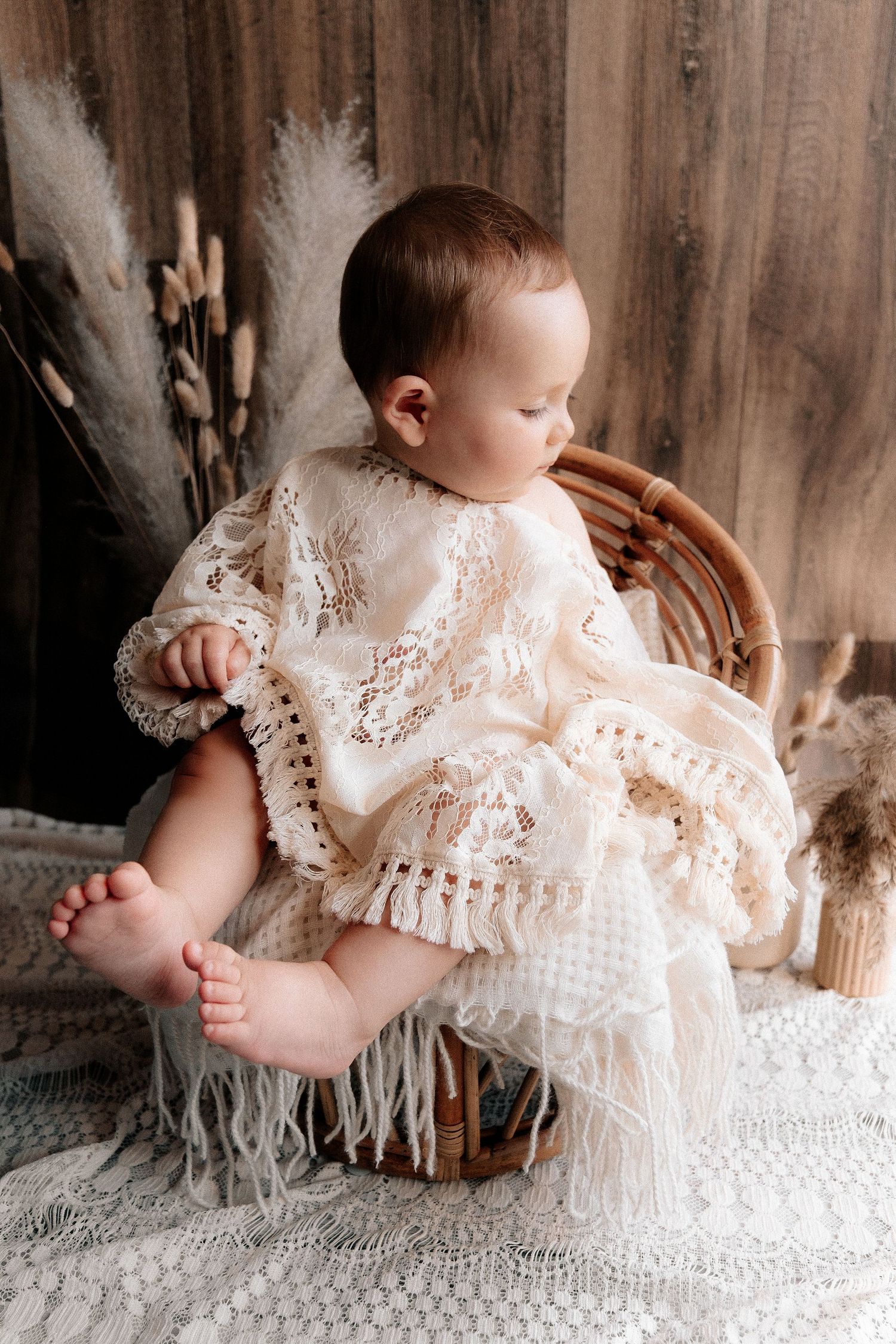Baby wearing delicate white lace dress on textured backdrop.