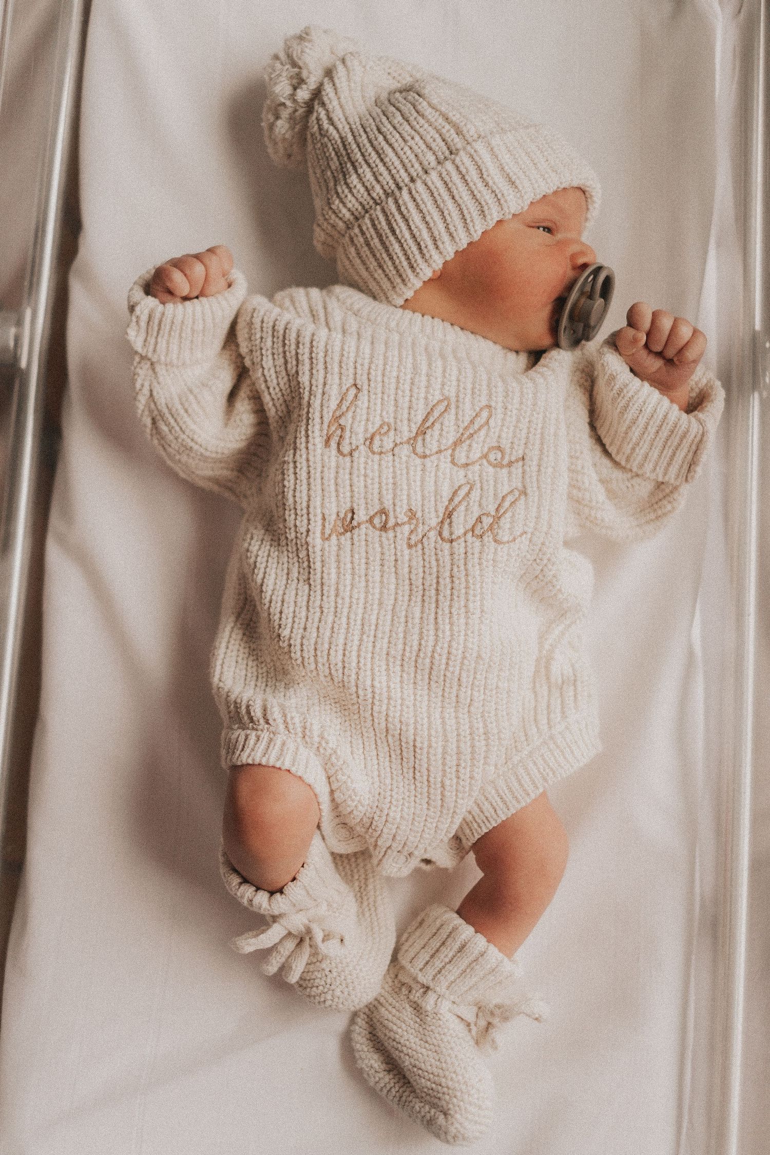 Newborn baby wearing cream knit outfit on white background.