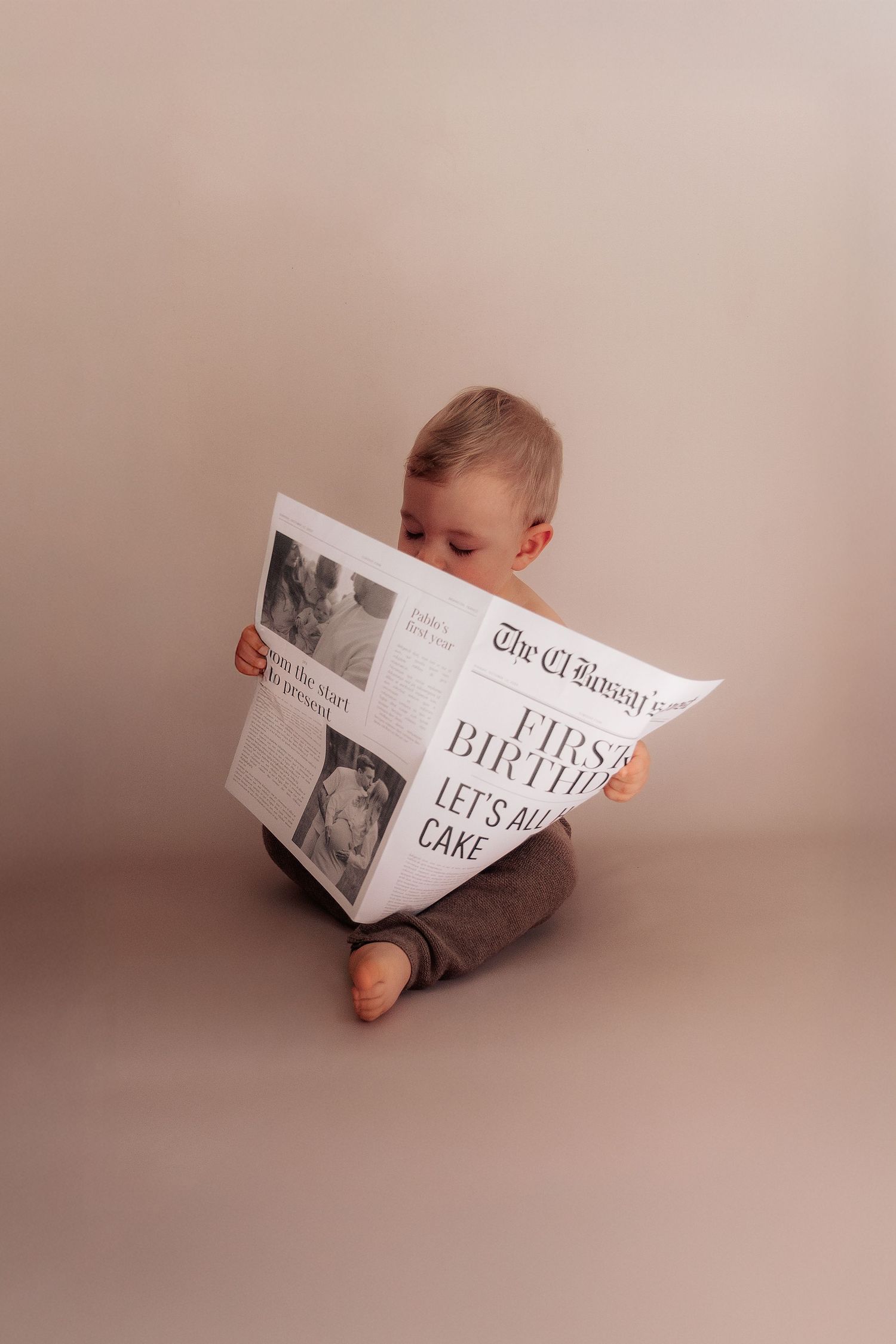 Baby lying on beige background looking at a book.