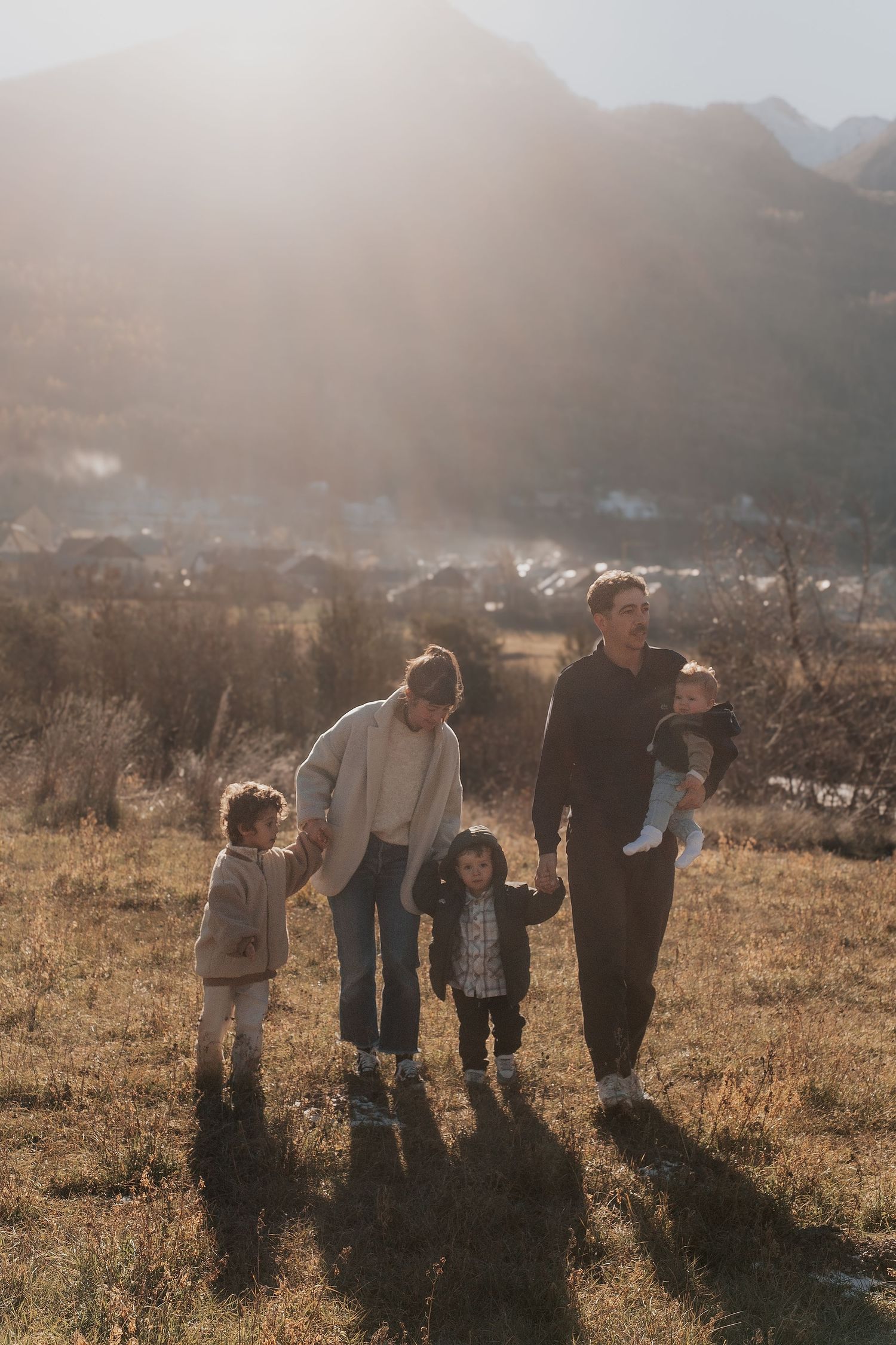 A group of people walk together across a sunlit field with mountains in the background during golden hour.