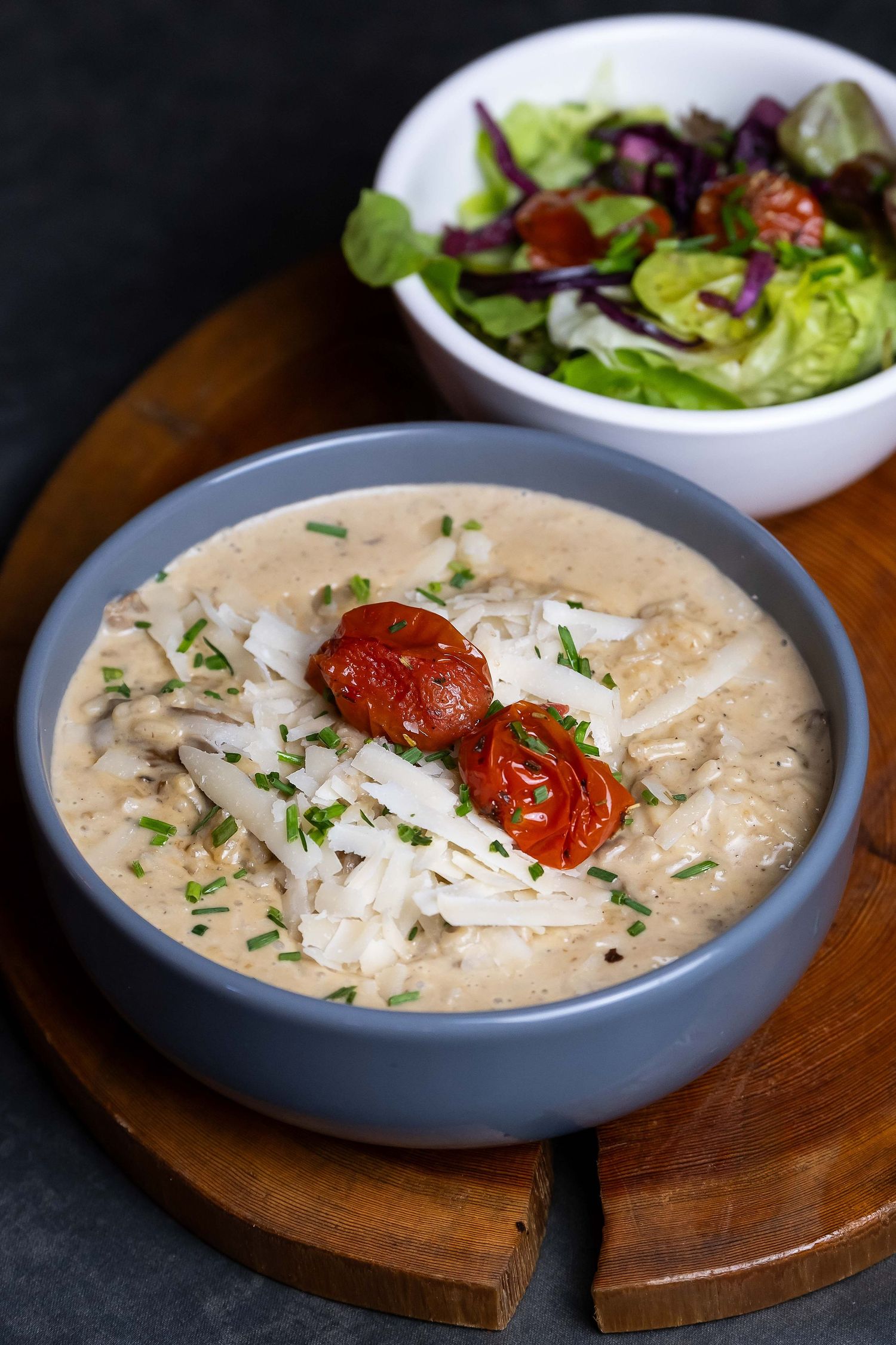 Creamy mushroom soup topped with roasted tomatoes and Parmesan, served with fresh garden salad on wooden board.