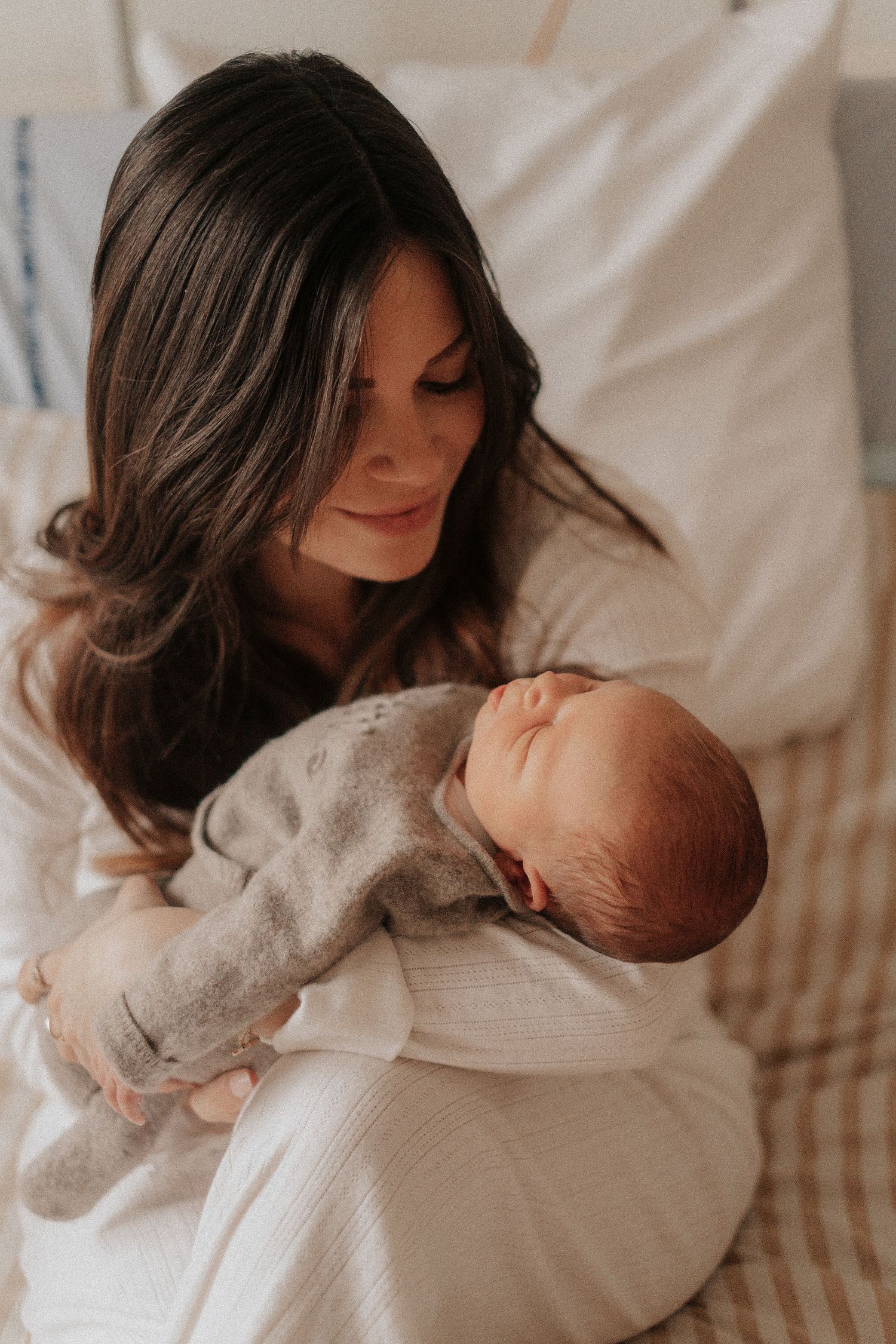 A tender moment between mother and newborn baby as they rest together on white bedding.