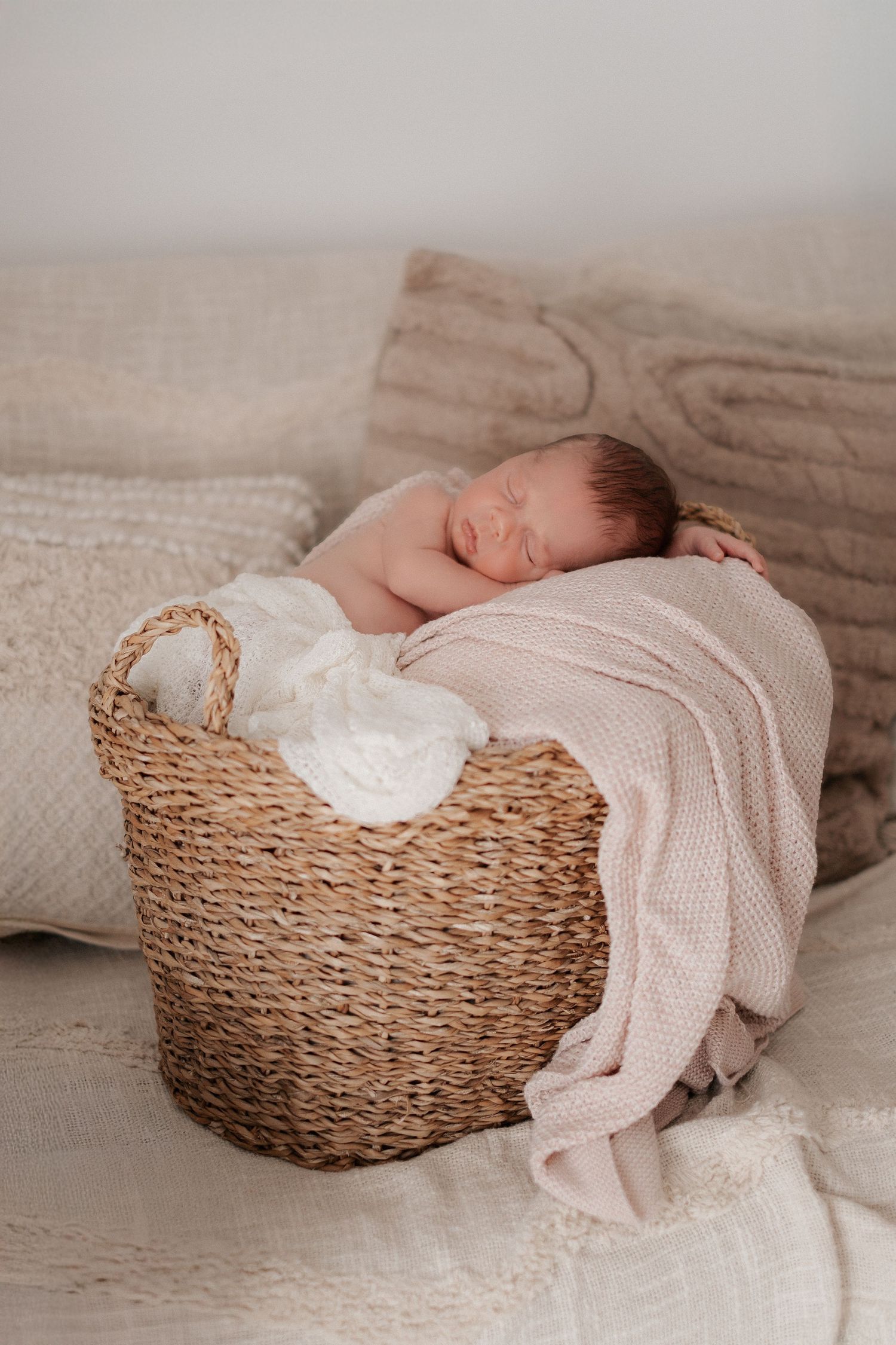 A newborn photography series showing a sleeping baby in a woven basket with soft pink blankets and white wraps.