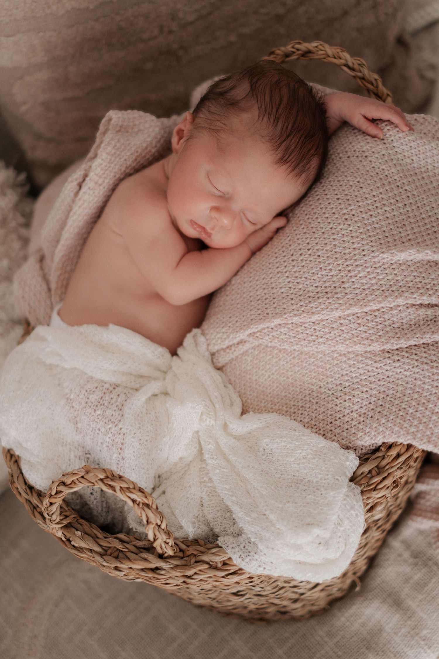 Sleeping newborn wrapped in white blanket resting in woven basket.