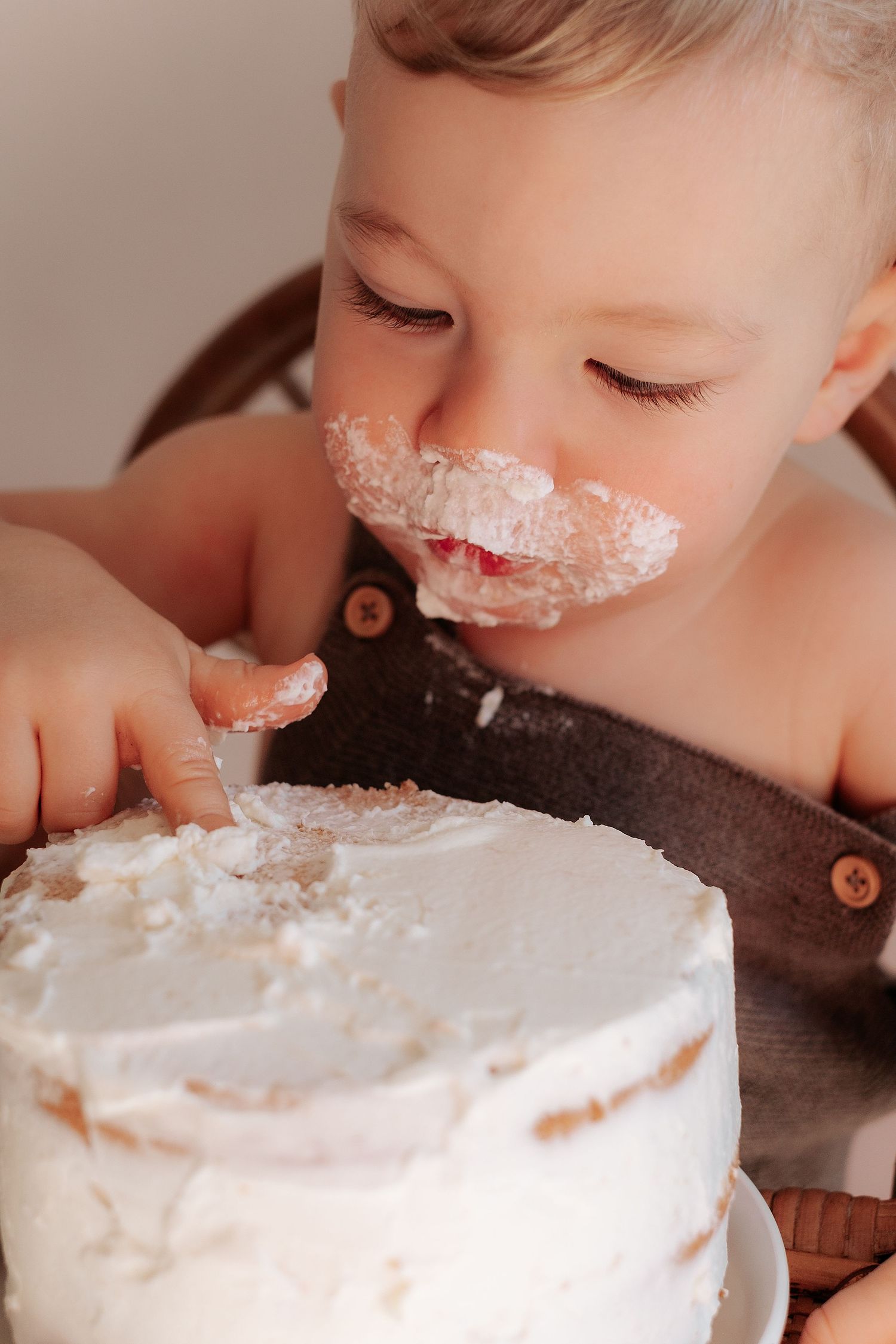 Baby enjoying first bite of birthday cake with frosting covered face.