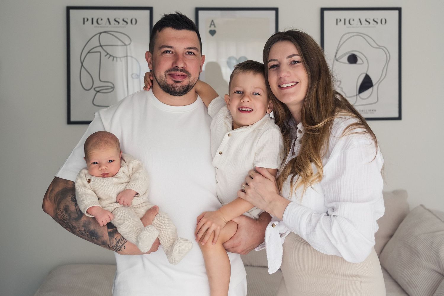 A family wearing white outfits poses together for portraits in front of Picasso artwork on a wall.