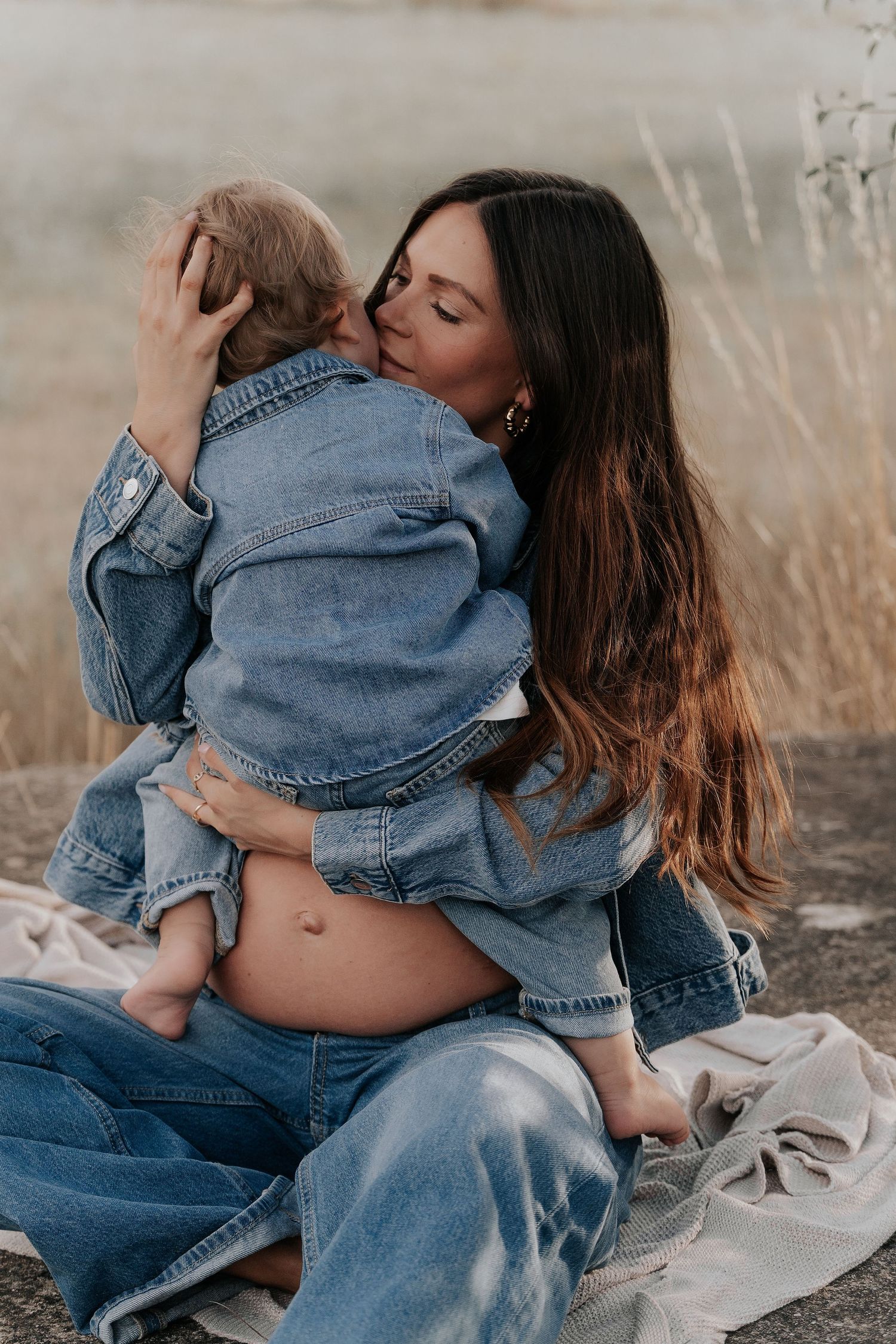 A tender moment between mother and baby wearing matching denim jackets while sitting outdoors in a natural setting.